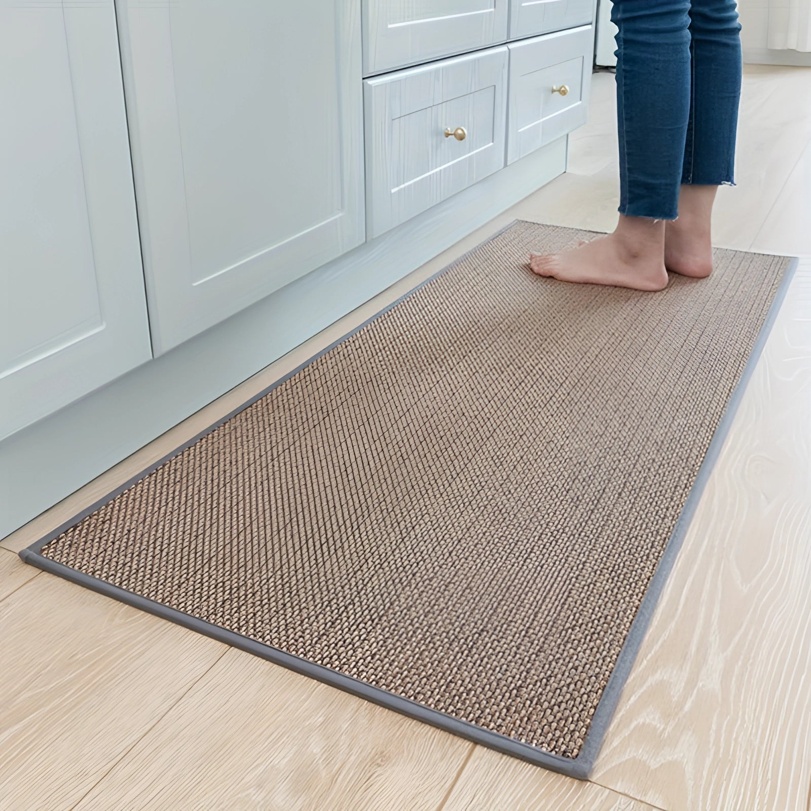 Beige kitchen mat in a gray beige color, measuring 50 x 120 cm, placed on a wooden or hardwood floor, featuring a non-slip surface and durable, washable sisal material. The mat is rectangular and complements the cabinetry in the background.