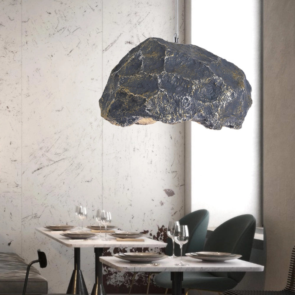 Organic stone pendant light hanging from the ceiling, illuminating a modern industrial interior space with wooden furniture and a rectangular window in the background.