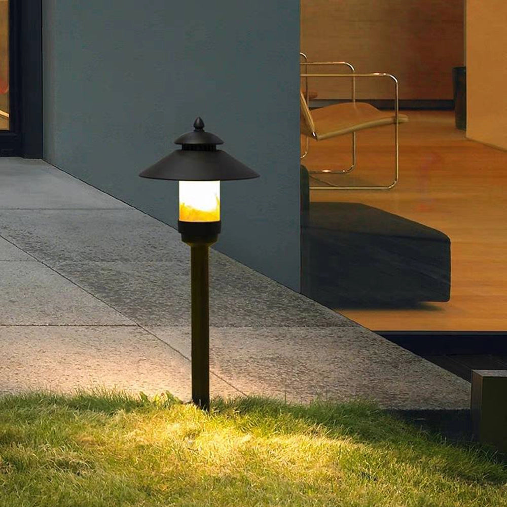 Pagoda-inspired outdoor path light illuminating a pathway, featuring a wooden base and a rectangular yellow shade, set against an asphalt road surface with surrounding grass.