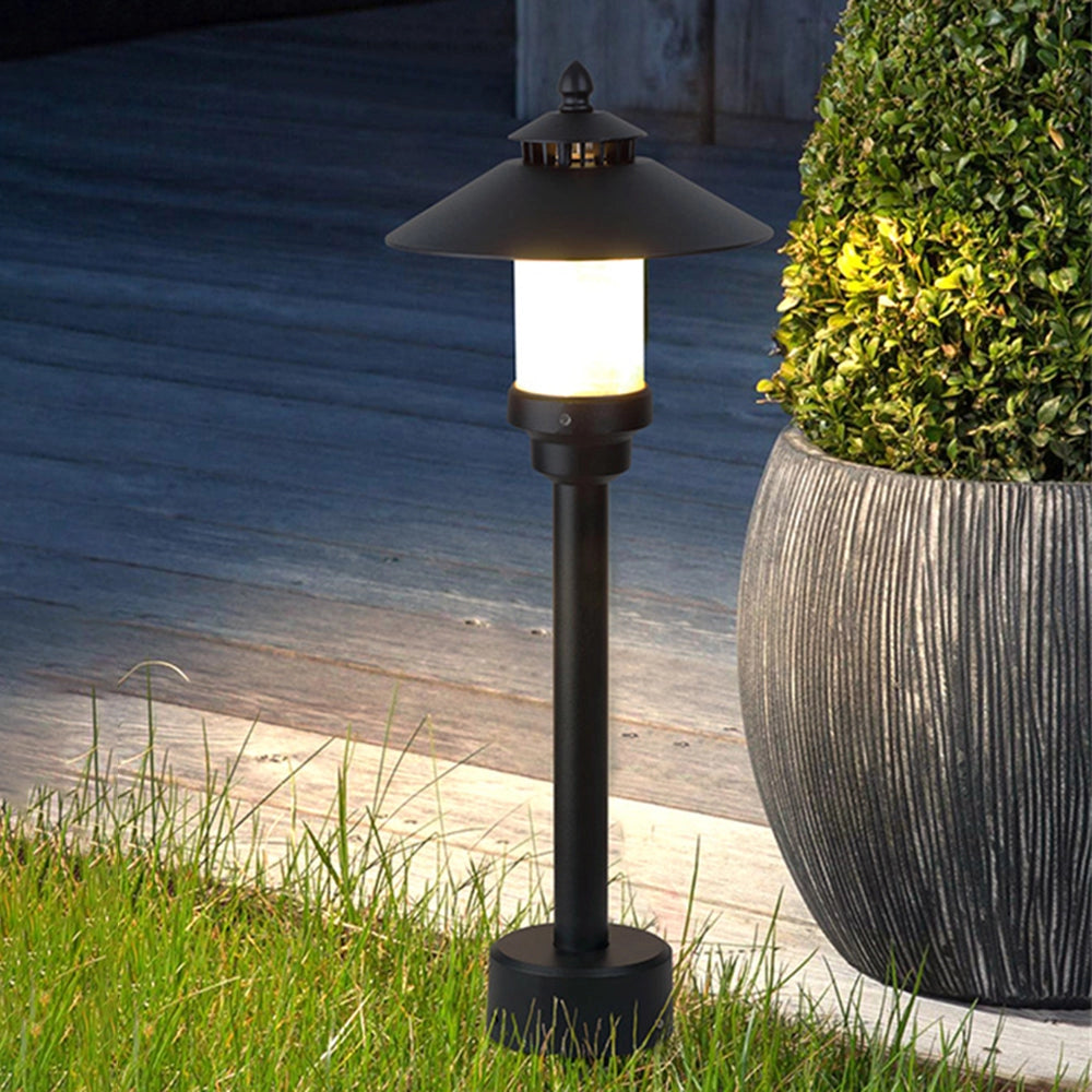 Pagoda-inspired weather-resistant outdoor path light illuminating a garden pathway, surrounded by grass and plants, with its warm glow casting artistic shadows.