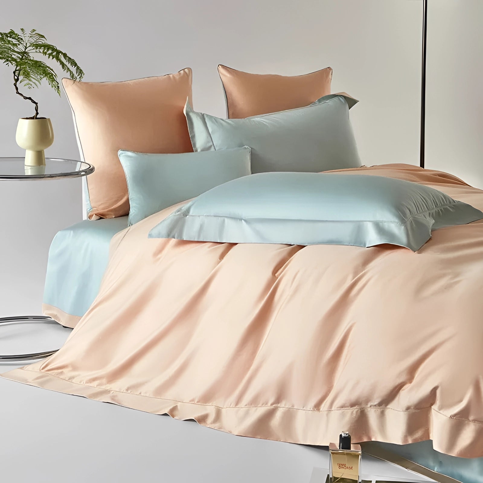 Pastel reversible satin duvet set in peach and aqua displayed on a bed with a wooden frame, featuring plush pillows and surrounded by potted plants for a cozy and comfortable bedroom ambiance.