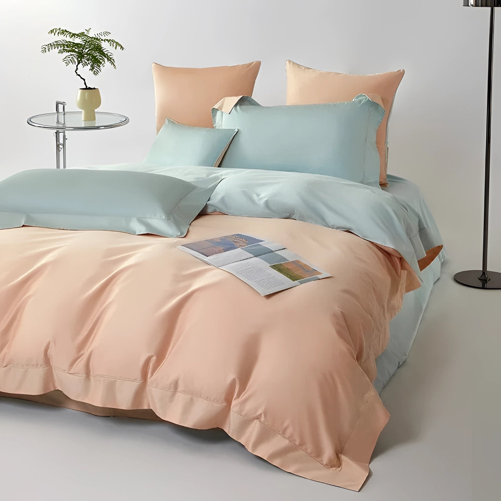 Reversible pastel satin duvet set in peach and aqua on a bed with matching pillows, featuring a light and airy design that complements the wooden floor and grey furniture in the room.