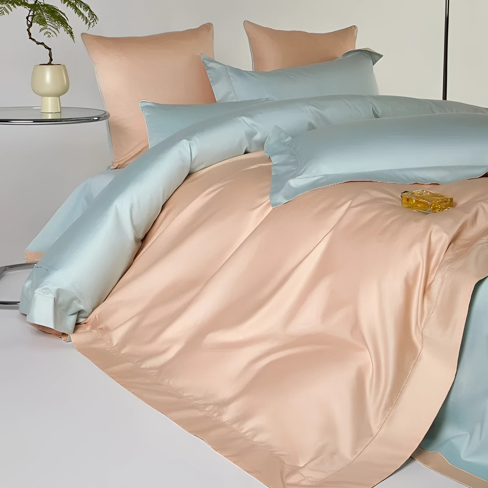Pastel reversible satin duvet set in peach and aqua colors displayed in a cozy bedroom setting, featuring soft bedding, pillows, and complemented by a lamp.
