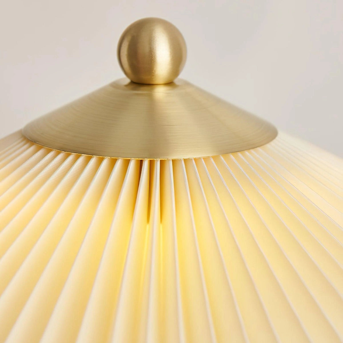 Pleated brass table lamp with a modern gold finish, featuring a pleated design and circular base, placed on a wooden surface.