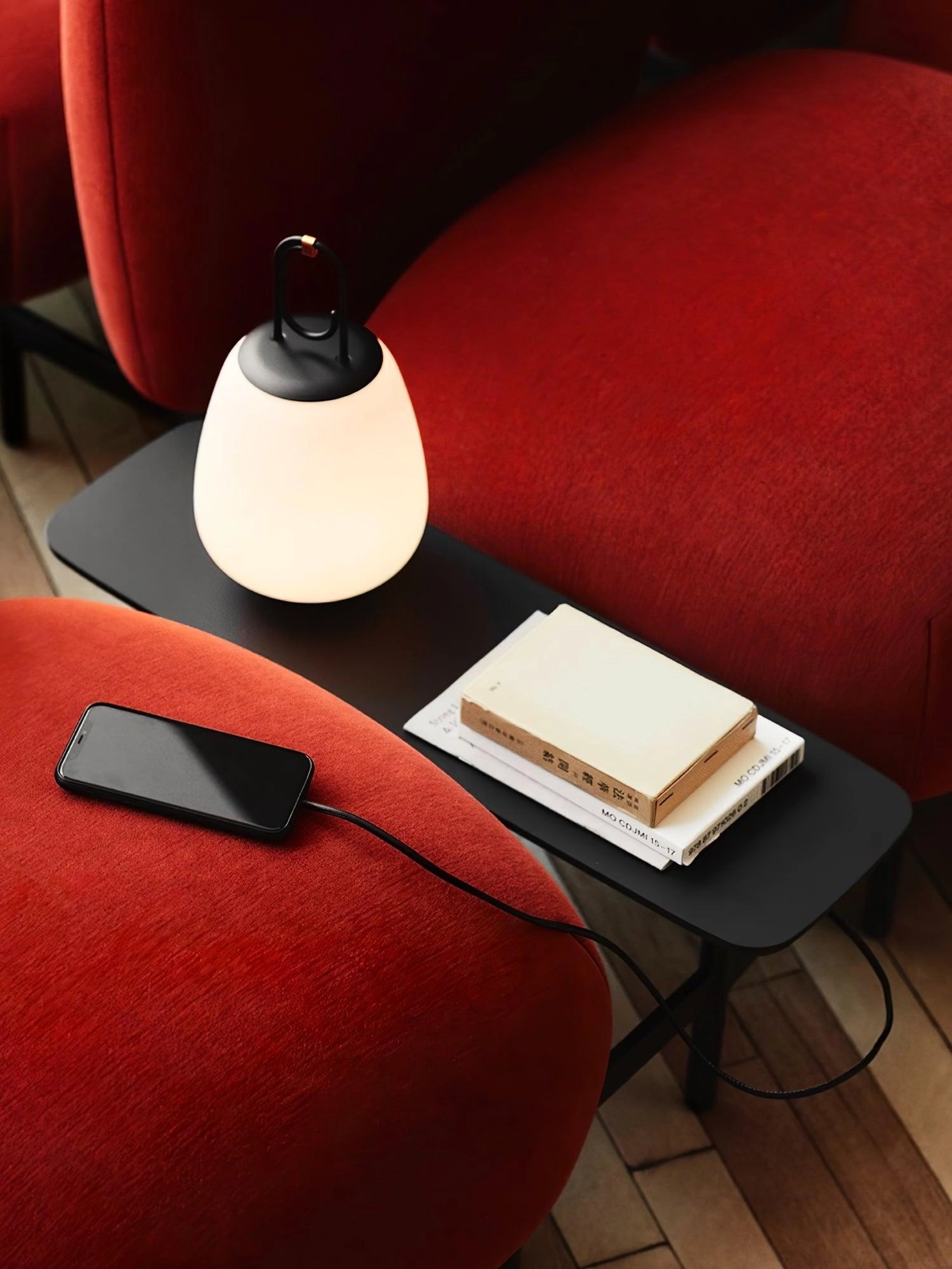 Portable rechargeable LED table lamp with a modern minimalist design, placed on a wooden table, providing comfortable lighting for indoor or outdoor settings, with a book nearby.