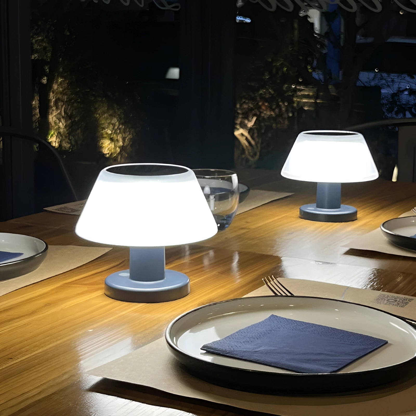 Rechargeable cordless LED table lamp with a modern design, featuring adjustable brightness and a blue base, placed on a wooden dining table with dishware.