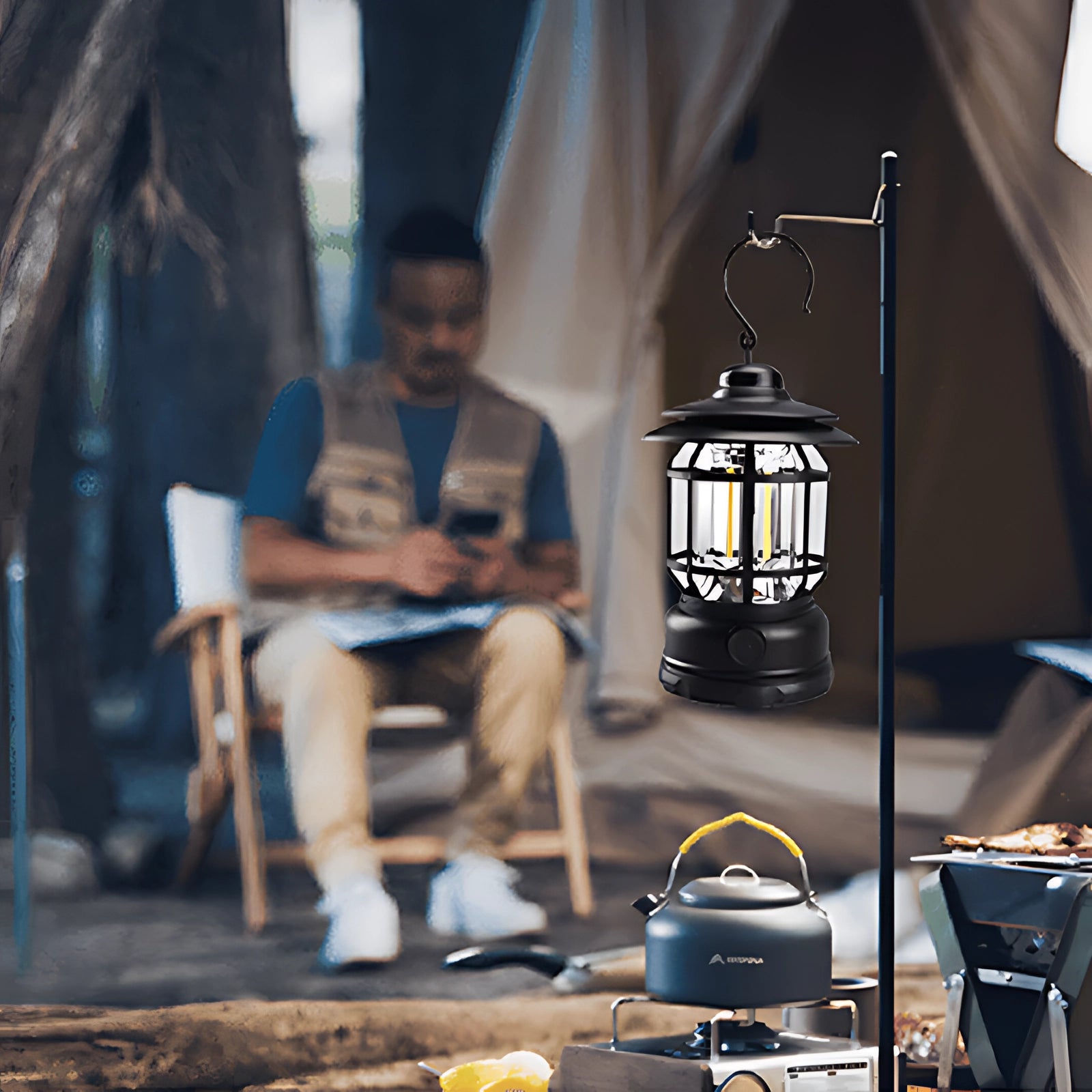 Rechargeable LED camping lantern placed on a table outdoors, providing light in a leisure setting with people sitting on chairs nearby. The scene suggests a relaxed, fun atmosphere, possibly at an event or outdoor gathering.