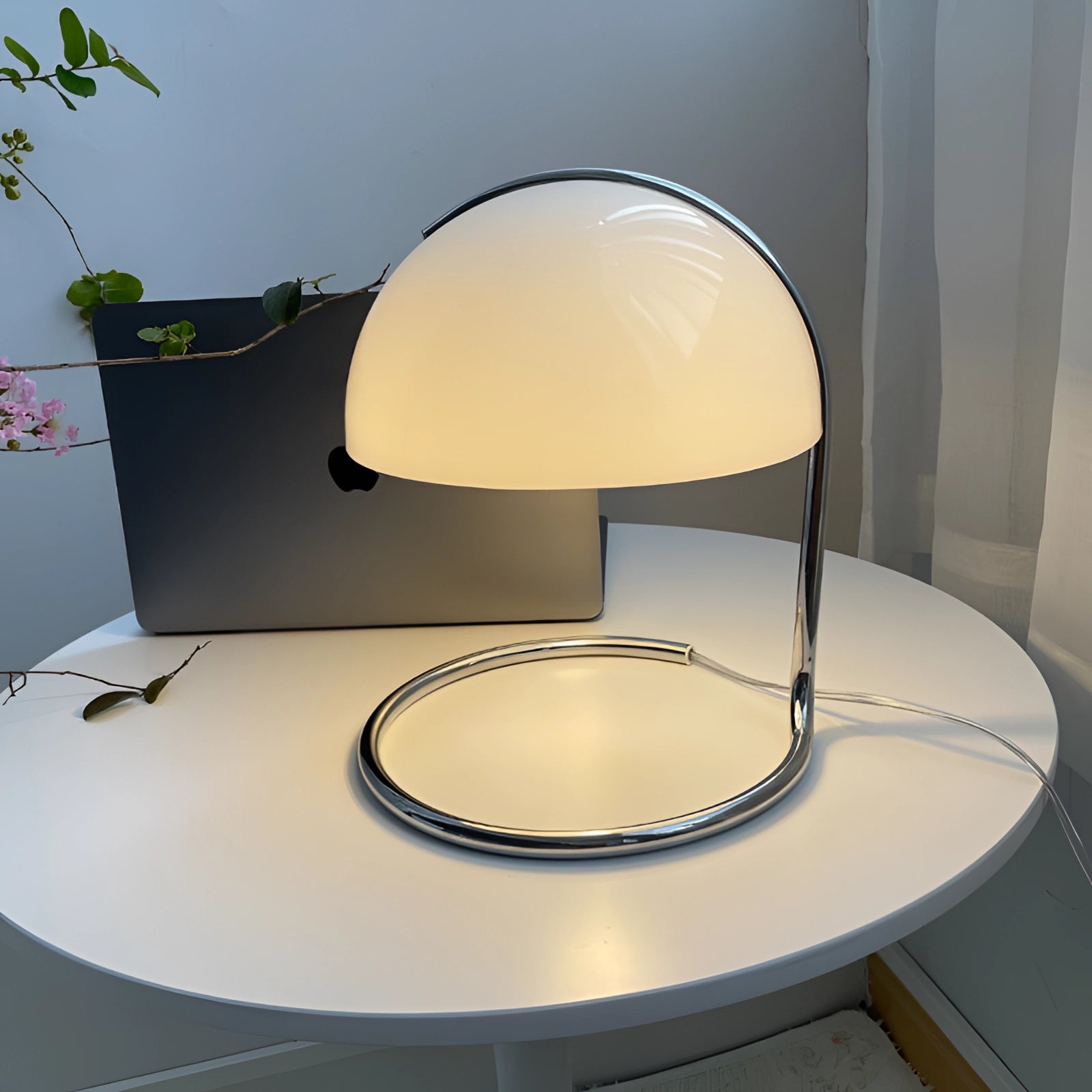 Retro yellow chrome mid-century desk lamp with an elegant design, featuring a round base and chrome finish, placed on a wooden table. The lamp emits a warm glow, adding a touch of vintage style to the setting.