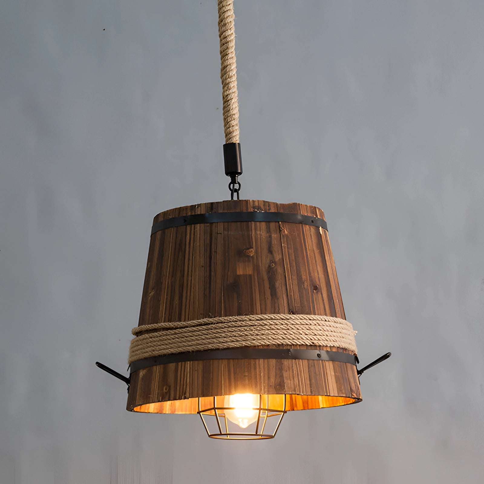 A rustic barrel pendant light featuring eco-friendly farmhouse design, hanging against a backdrop of a cloudy sky. The metal and composite material fixture showcases tints and shades, adding to the aesthetic appeal of the lighting accessory.