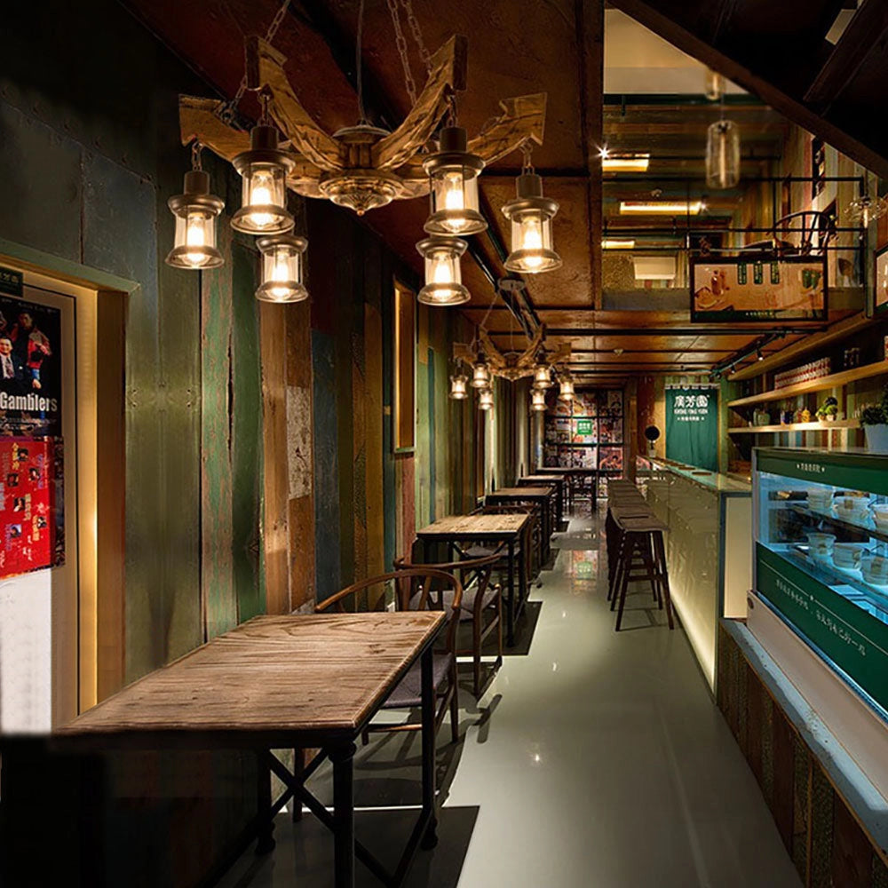 Rustic metal and wood chandelier hanging from the ceiling in a cozy cabin interior, surrounded by wooden furniture and decor elements like tables and shelves.