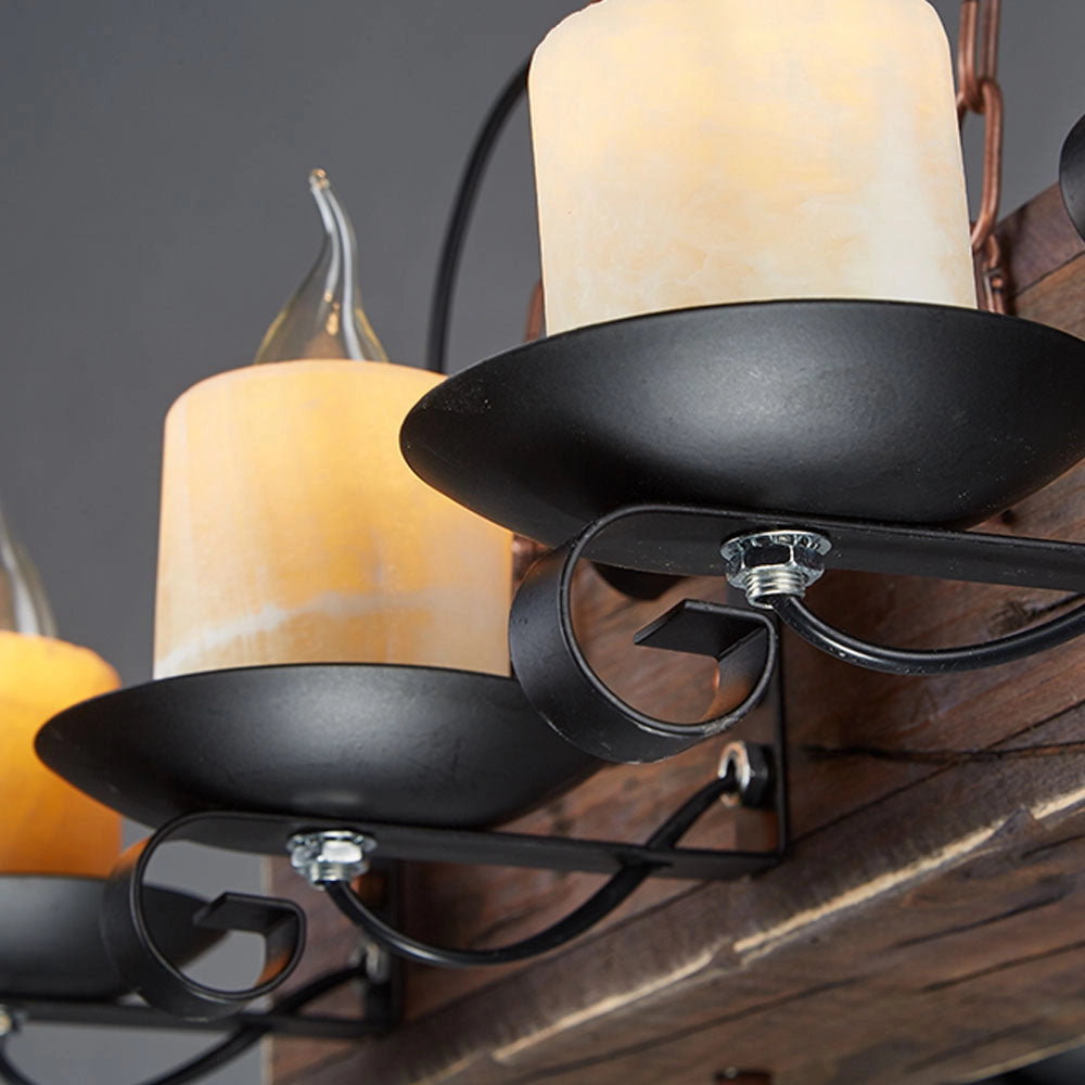 Rustic wooden beam chandelier with an antique bronze finish, featuring metal accents and a light fixture that casts a warm glow, set against a backdrop of chairs and wood elements.