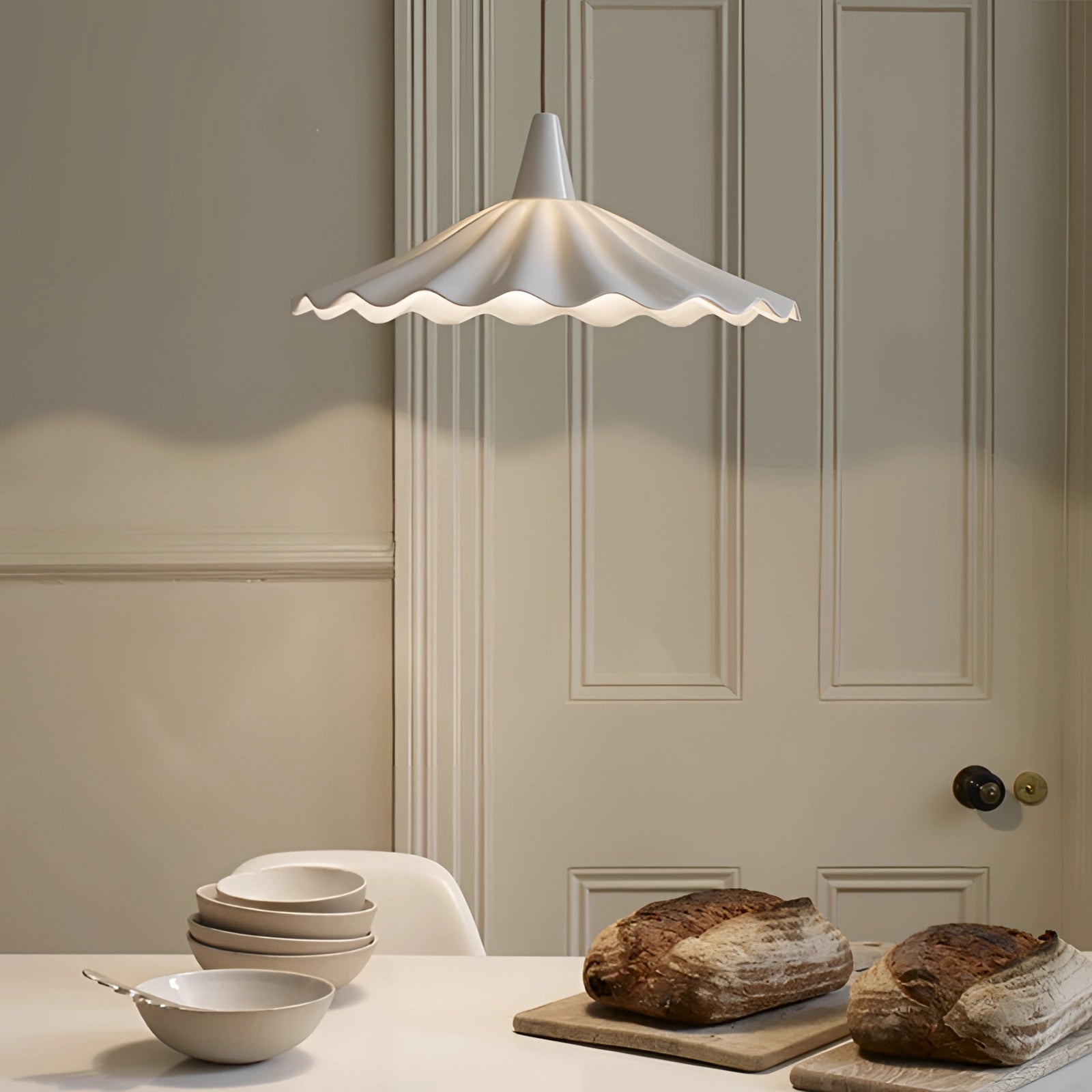 Modern scallop-edged LED pendant light with a decorative design, hanging over a wooden table set with tableware, including plates, cups, and serveware, creating an elegant and contemporary interior.