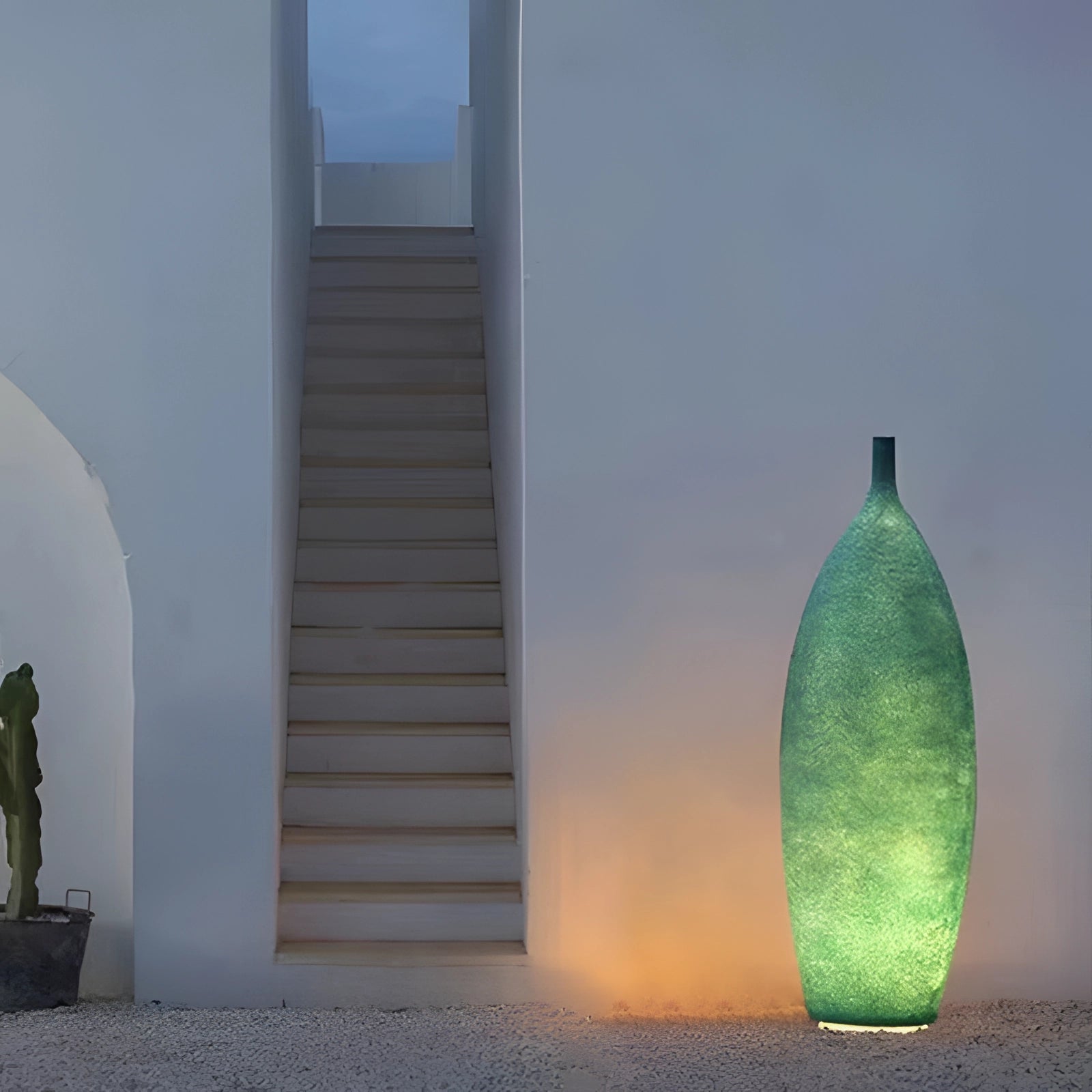Scandinavian minimalist tall narrow green ceramic vase with distressed finish, standing 36.5 inches tall, placed in front of a muted wall with subtle art and wooden accents in the background.