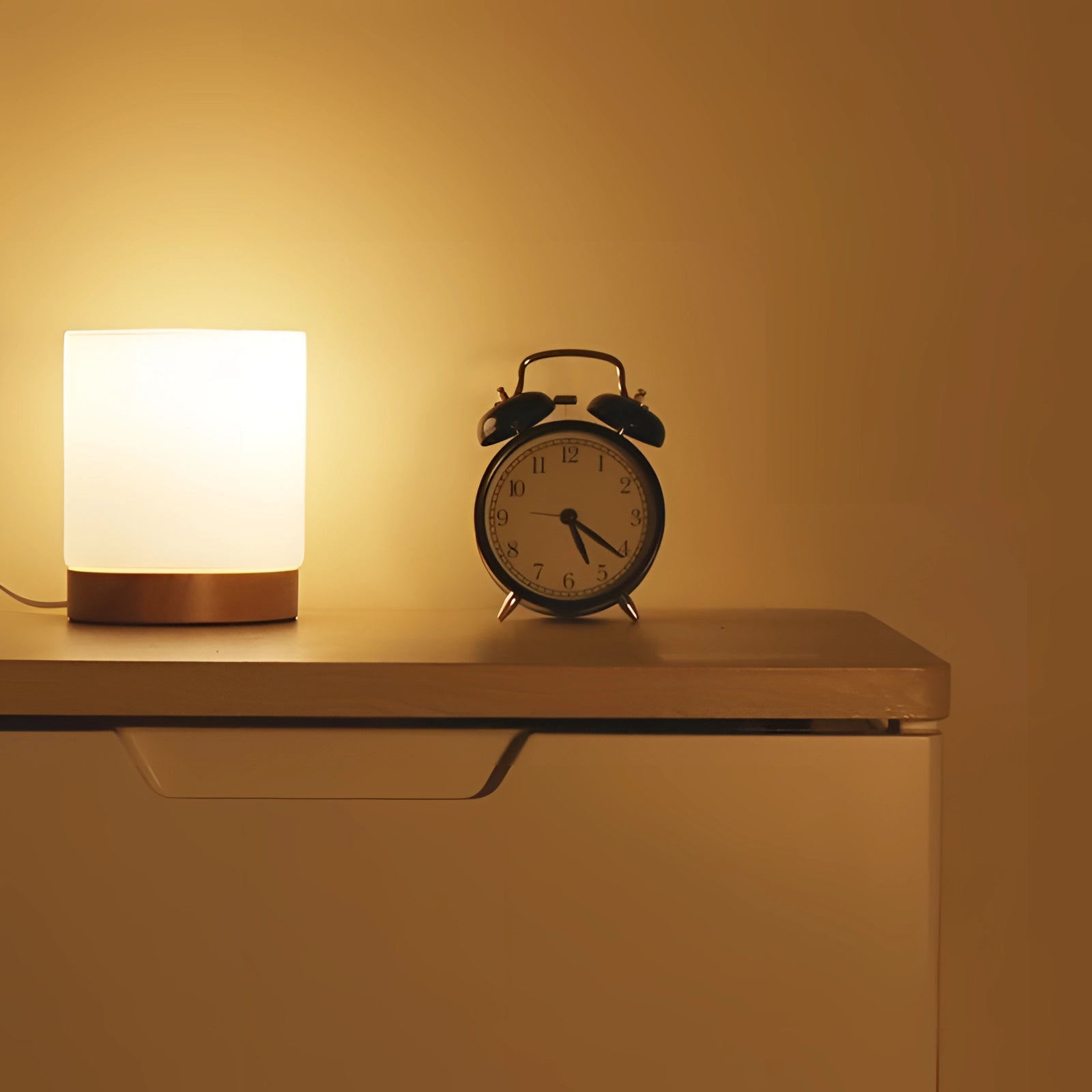 Scandinavian minimalist table lamp with a wooden base and rectangular warm LED light, placed on a wooden shelf beside an alarm clock.
