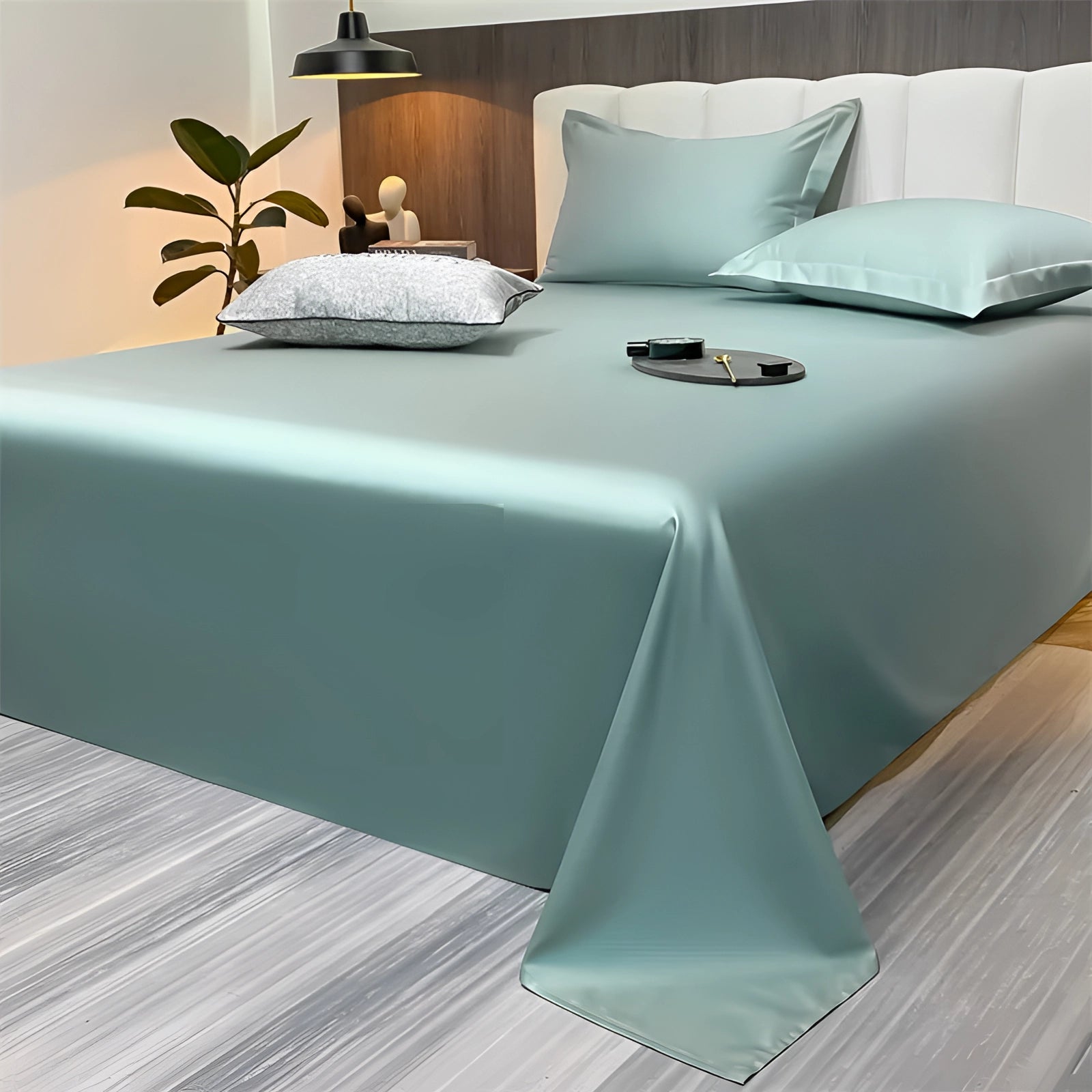 Sea green silky luxury bed sheets in a light green shade are elegantly spread across a bed in a modern minimalist bedroom decor. The sheets, sized 245x265cm, exude a smooth and shiny texture, enhancing the room's serene ambiance. The surrounding decor is simple, with muted tones of white and grey, emphasizing the sheets' luxurious appeal.