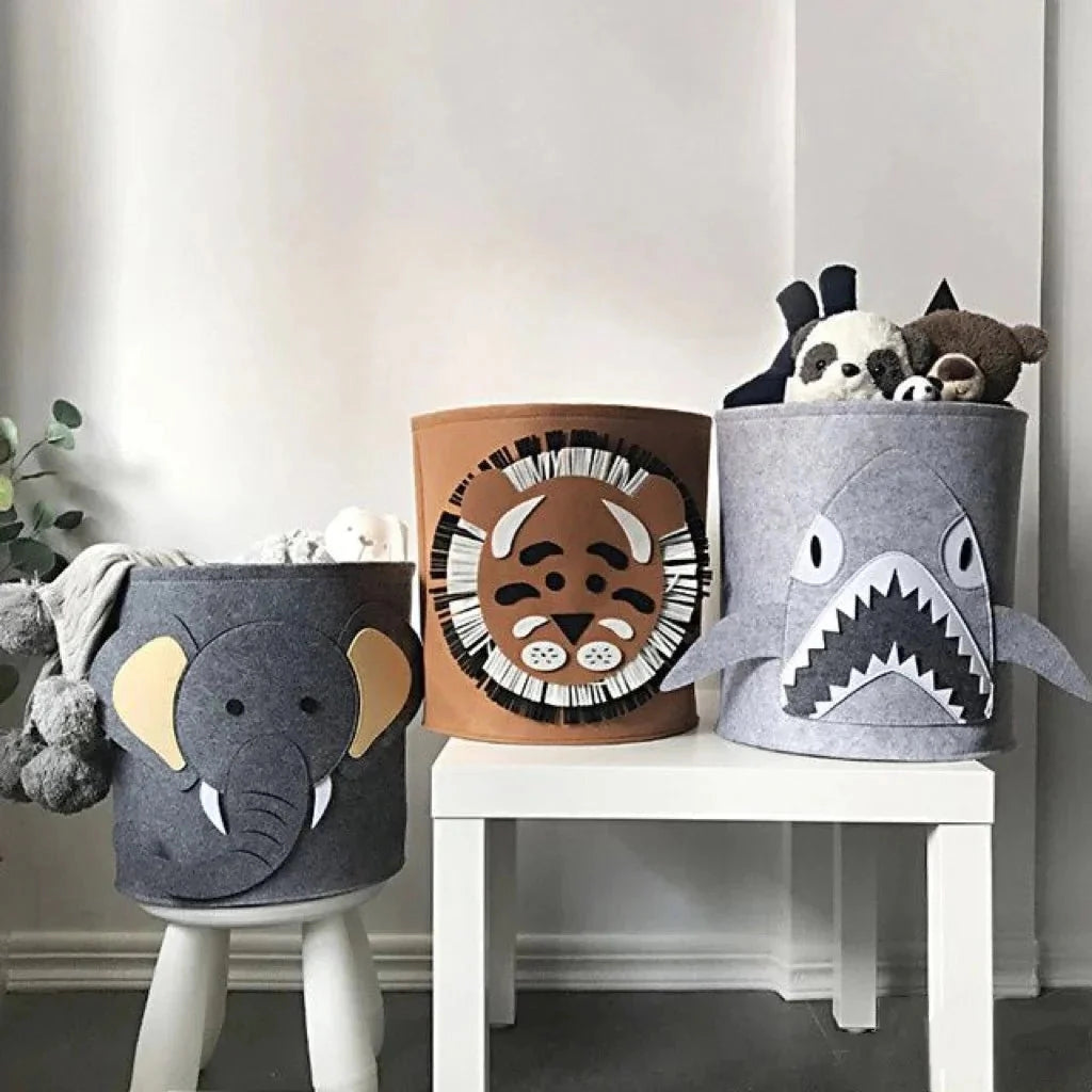 Gray shark-shaped felt basket used as a kids' toy storage organizer, placed on a shelf alongside houseplants and flowerpots.