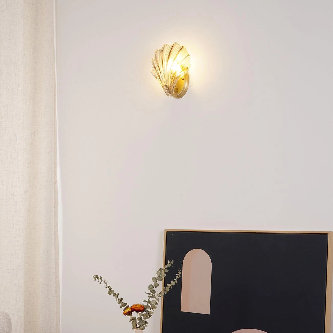 Gold shell wall sconce with a coastal nautical design mounted on a wooden panel, surrounded by decorative plants and twigs.