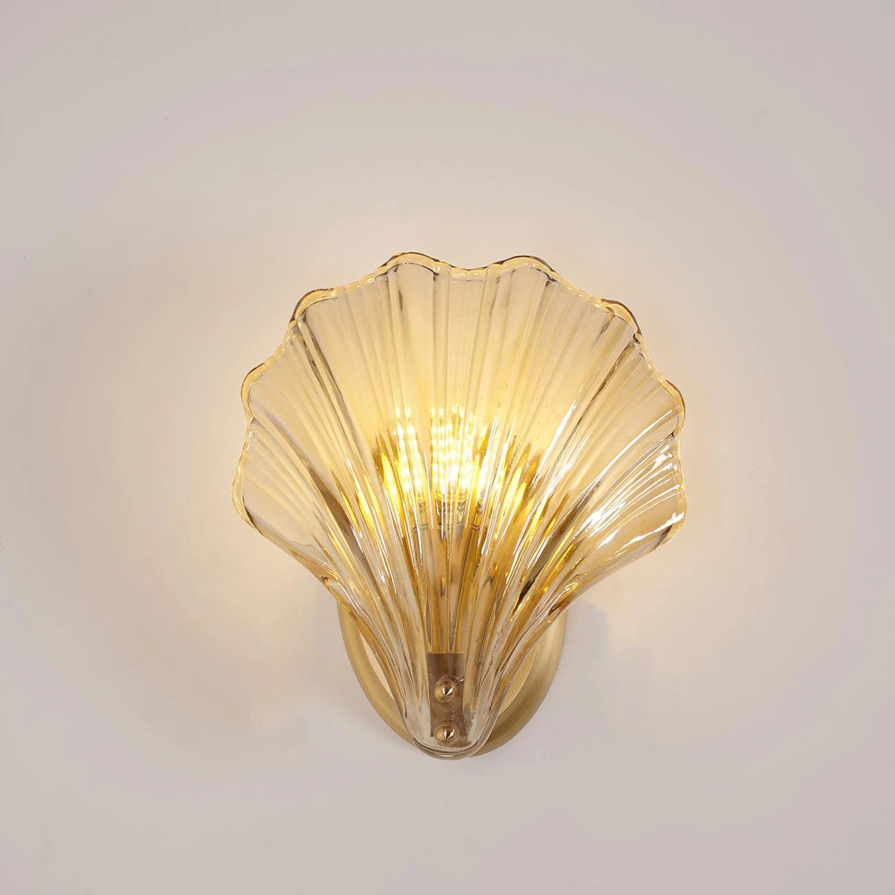 Gold nautical coastal seashell light fixture mounted on a white wall, featuring intricate shell design with metallic finish, illuminating the space with a warm glow.