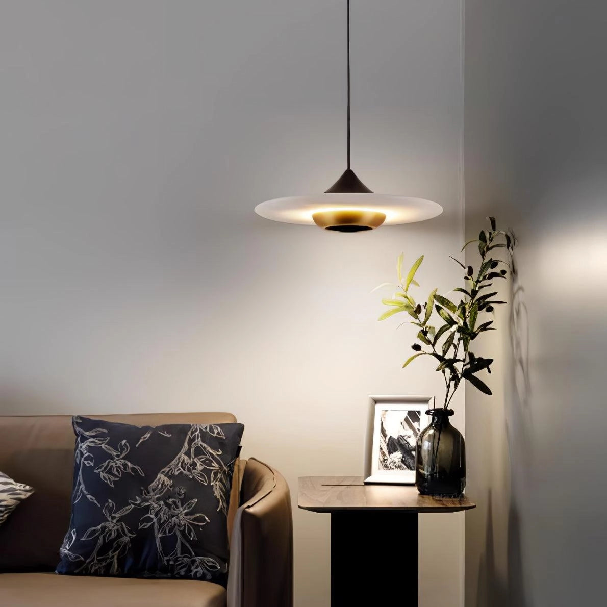 Sleek black LED pendant light hanging from the ceiling, illuminating a modern minimalist interior space featuring a wooden floor, potted houseplants, and a cozy ambiance.