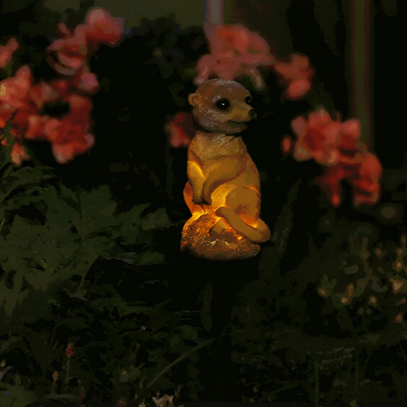 Solar LED meerkat garden light in the shape of a meerkat, designed for outdoor use. The meerkat is standing amidst grass and flowers, making it an ideal lawn ornament. The design is whimsical, resembling a toy or Easter bunny, perfect for adding charm to garden decor.