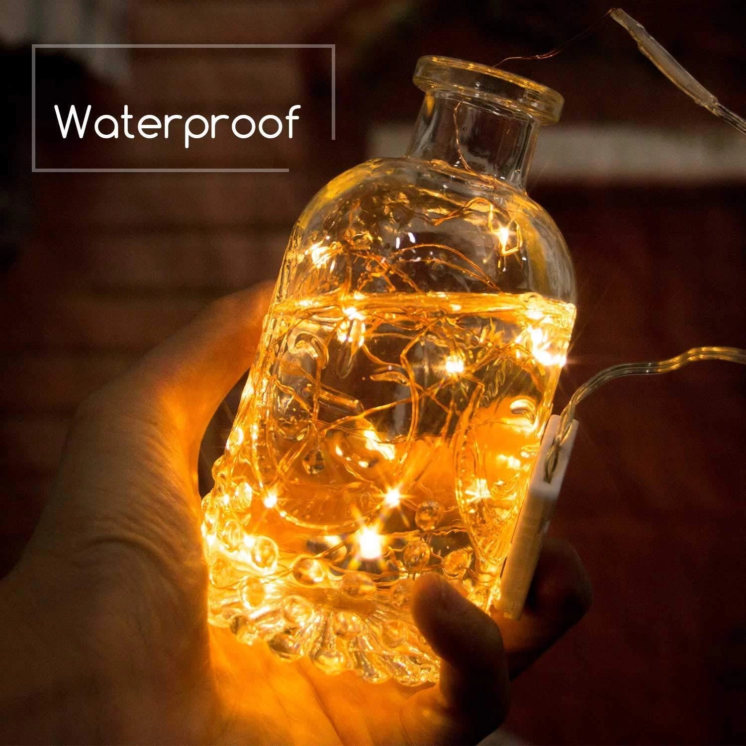 Solar powered outdoor LED fairy lights wrapped around a clear glass bottle, creating a warm amber glow, showcasing the waterproof and eco-friendly design suitable for various outdoor settings.
