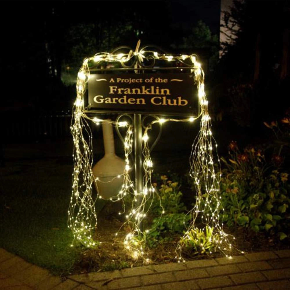 Solar powered outdoor LED fairy lights illuminating a garden area at night, surrounded by grass and plants, showcasing eco-friendly and waterproof features.