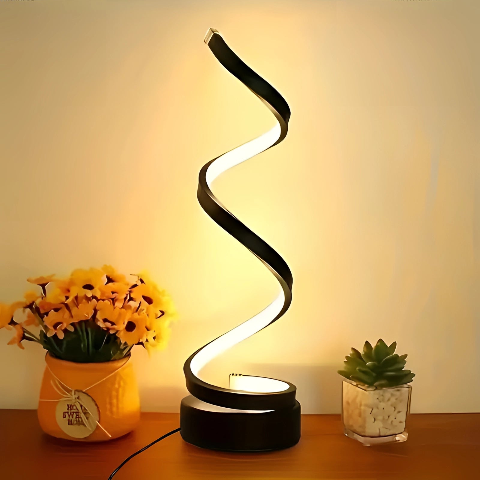 Spiral LED desk lamp with a modern minimalist sculptural design placed on a wooden table, surrounded by various houseplants and a decorative vase, enhancing the interior design.