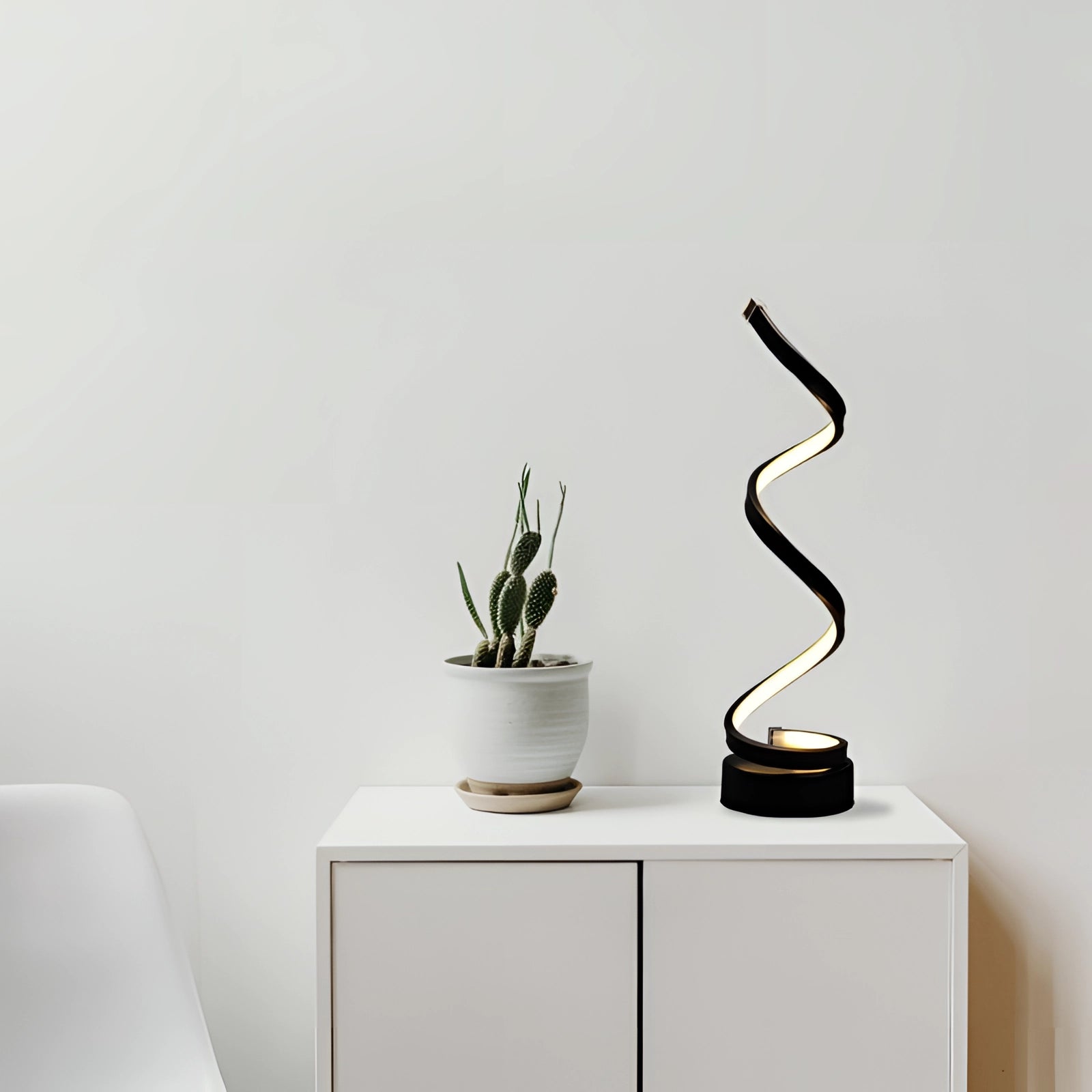 Modern minimalist desk setup featuring a black spiral LED desk lamp, surrounded by a wooden vase with a houseplant, set on a sleek hardwood surface in a contemporary interior design environment.