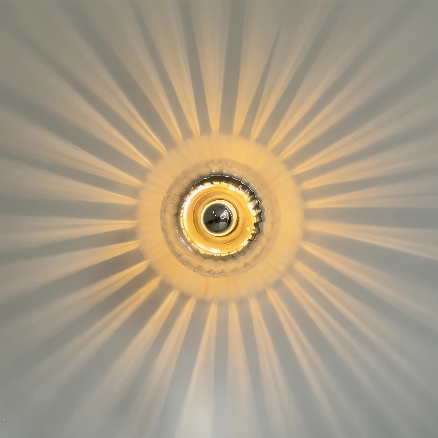 Modern gold radial pattern ceiling light fixture with a symmetrical sunburst design, featuring a circular shape and artistic elements, mounted on a ceiling.