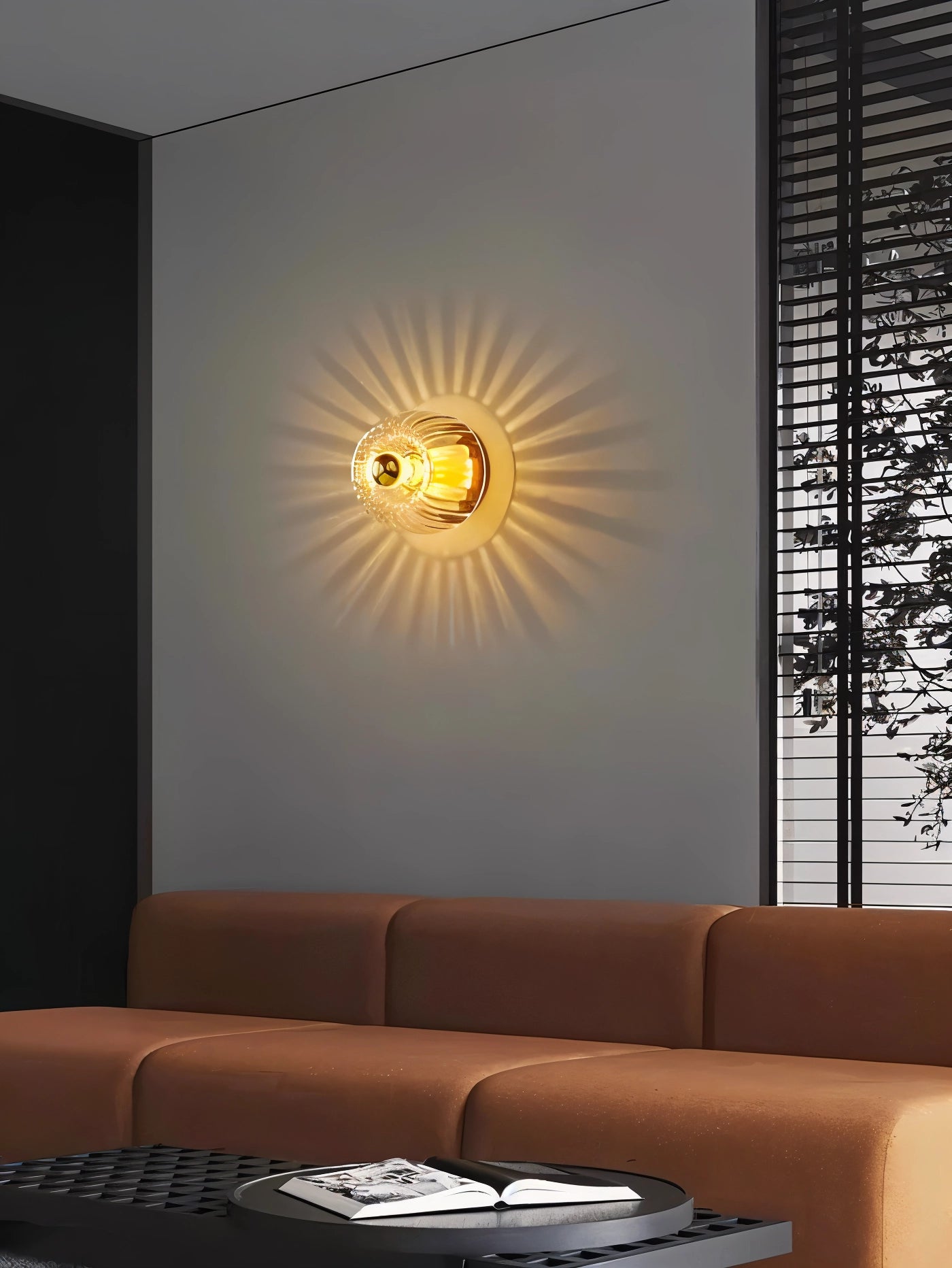 Modern room interior featuring a sunburst ceiling light with a gold radial pattern fixture illuminating a cozy space. The room includes a brown couch and wooden furniture elements, creating a warm and inviting atmosphere.