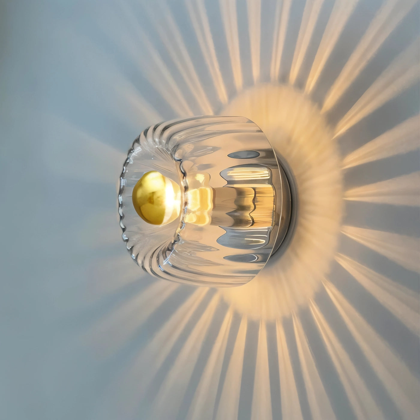 Modern gold ceiling light fixture with a radial sunburst pattern, featuring symmetrical design elements and a close-up view of its artistic circular form, set against a ceiling backdrop.