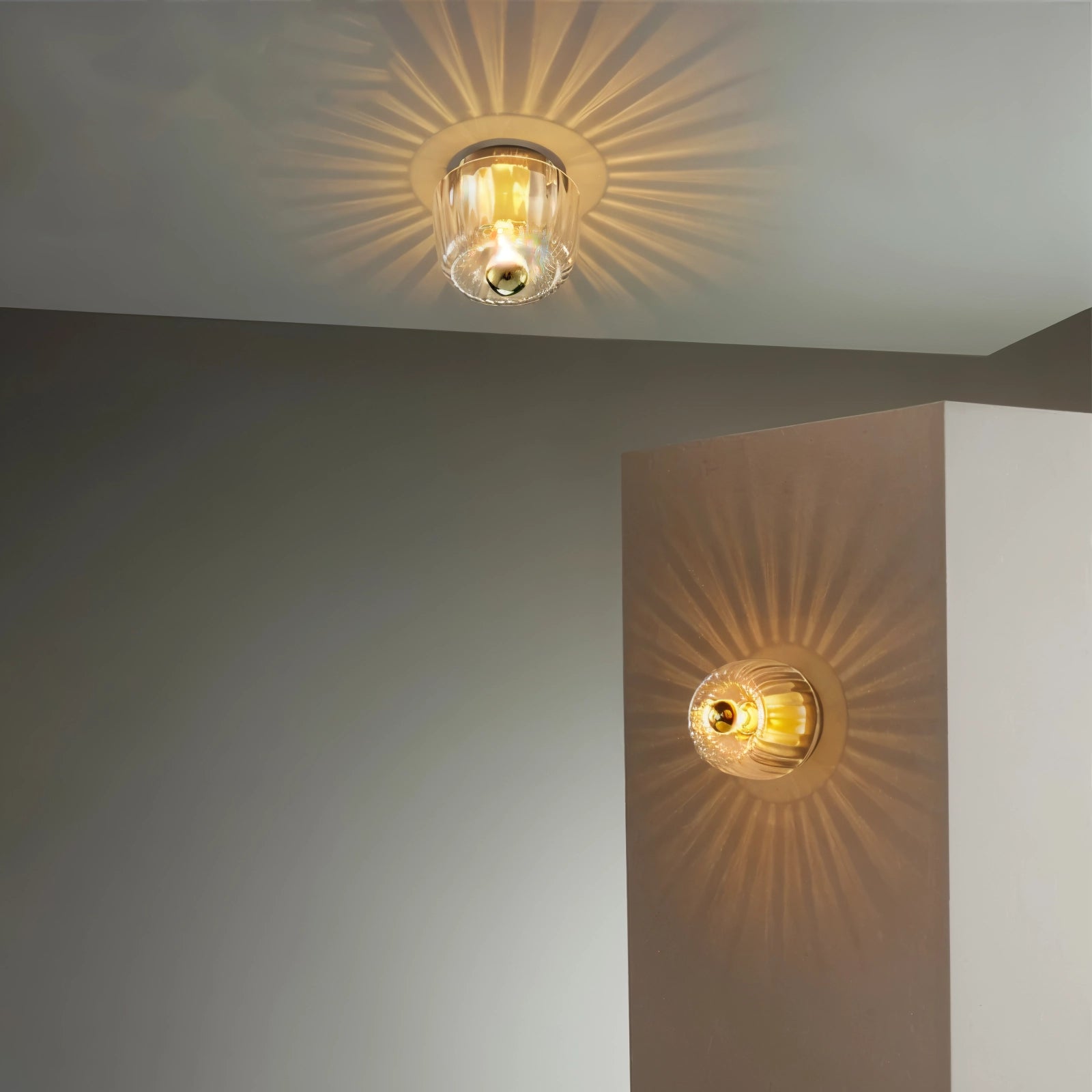 Modern gold sunburst ceiling light fixture with a radial pattern, featuring amber and wood tones, mounted on a ceiling.