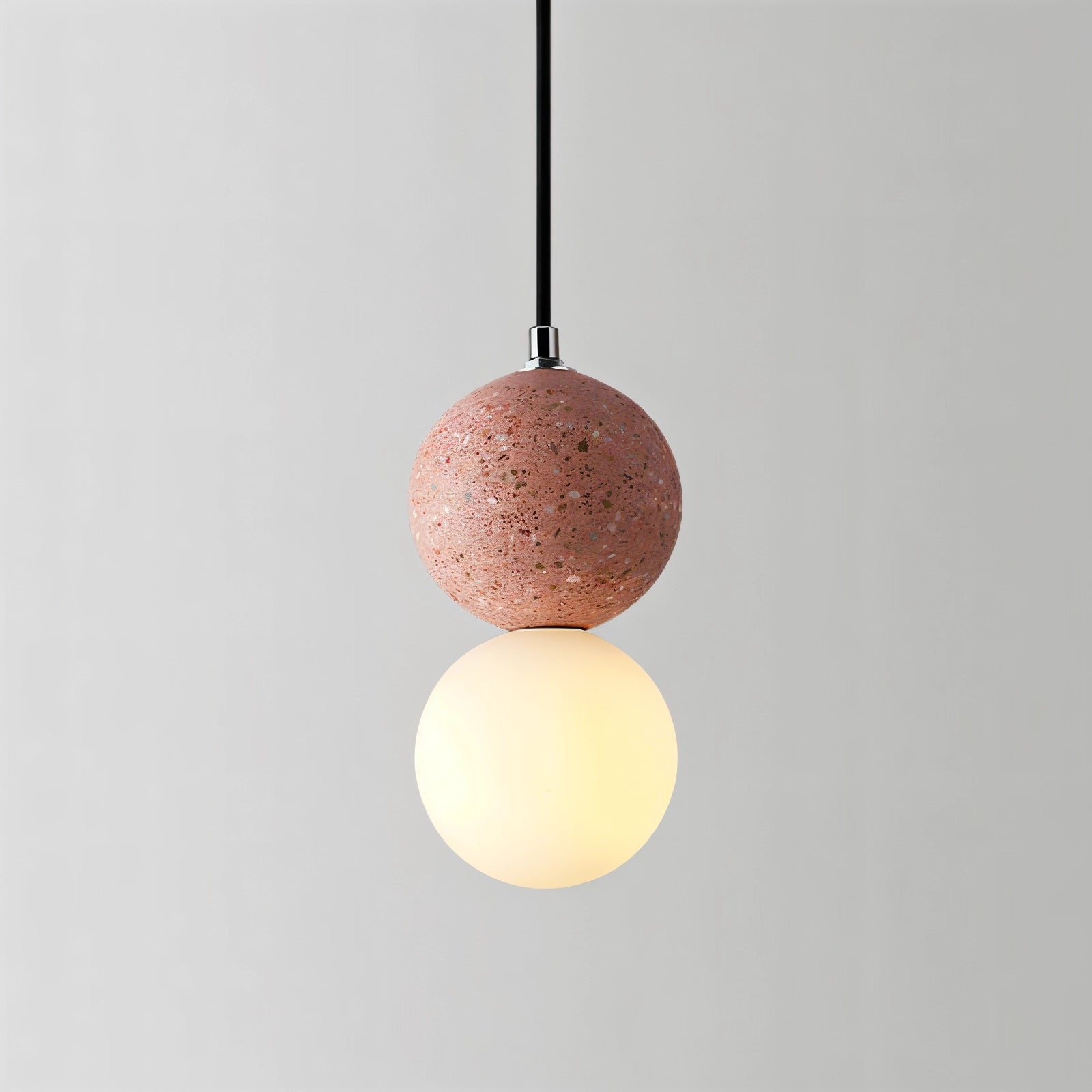 Spherical pendant light with a terrazzo design, featuring a minimalist concrete fixture in a pink tint, hanging from the ceiling in an interior setting.