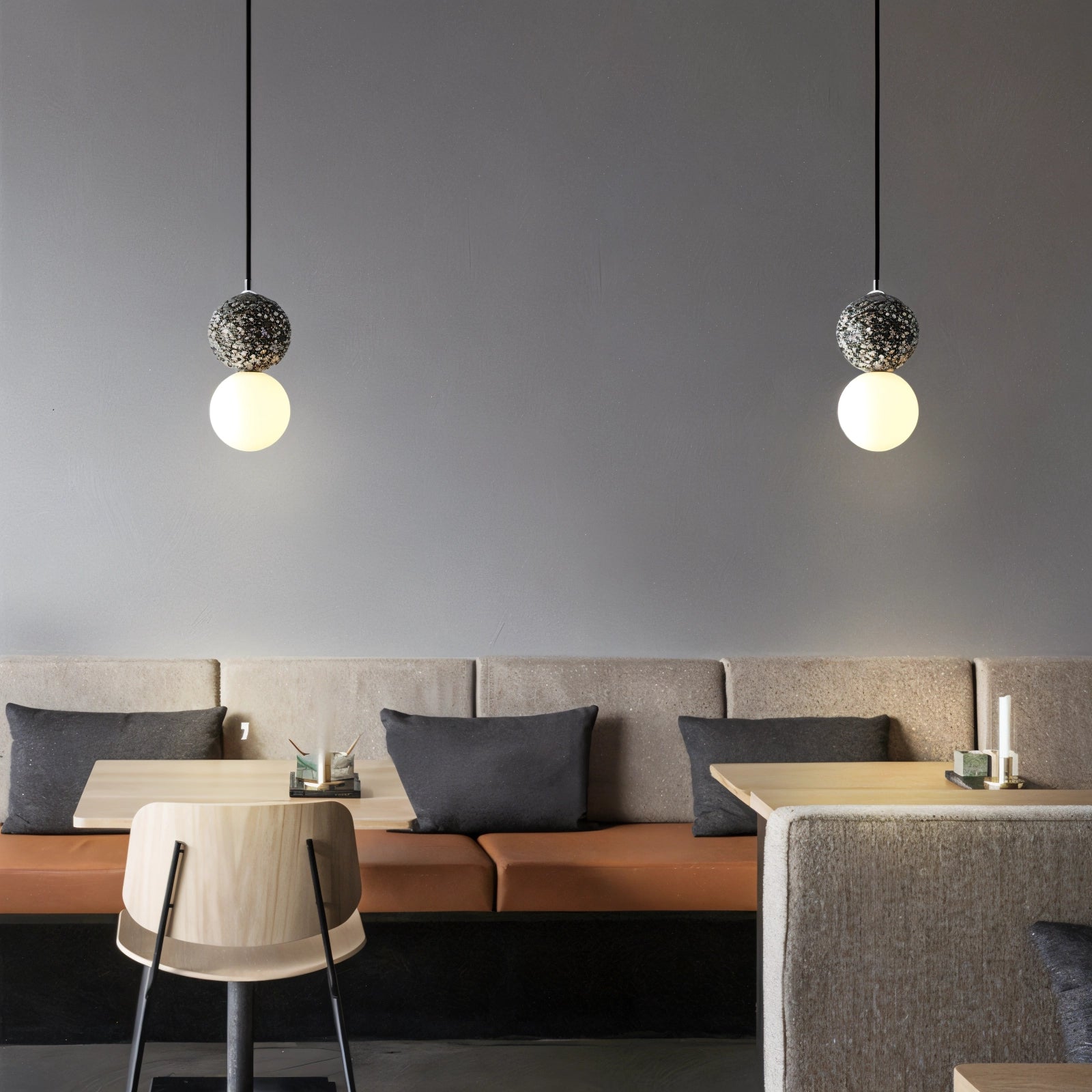 A spherical pendant light made of terrazzo concrete, featuring a minimalist design, hangs from the ceiling. The fixture casts a soft glow, illuminating a stylish interior with wooden and grey elements.