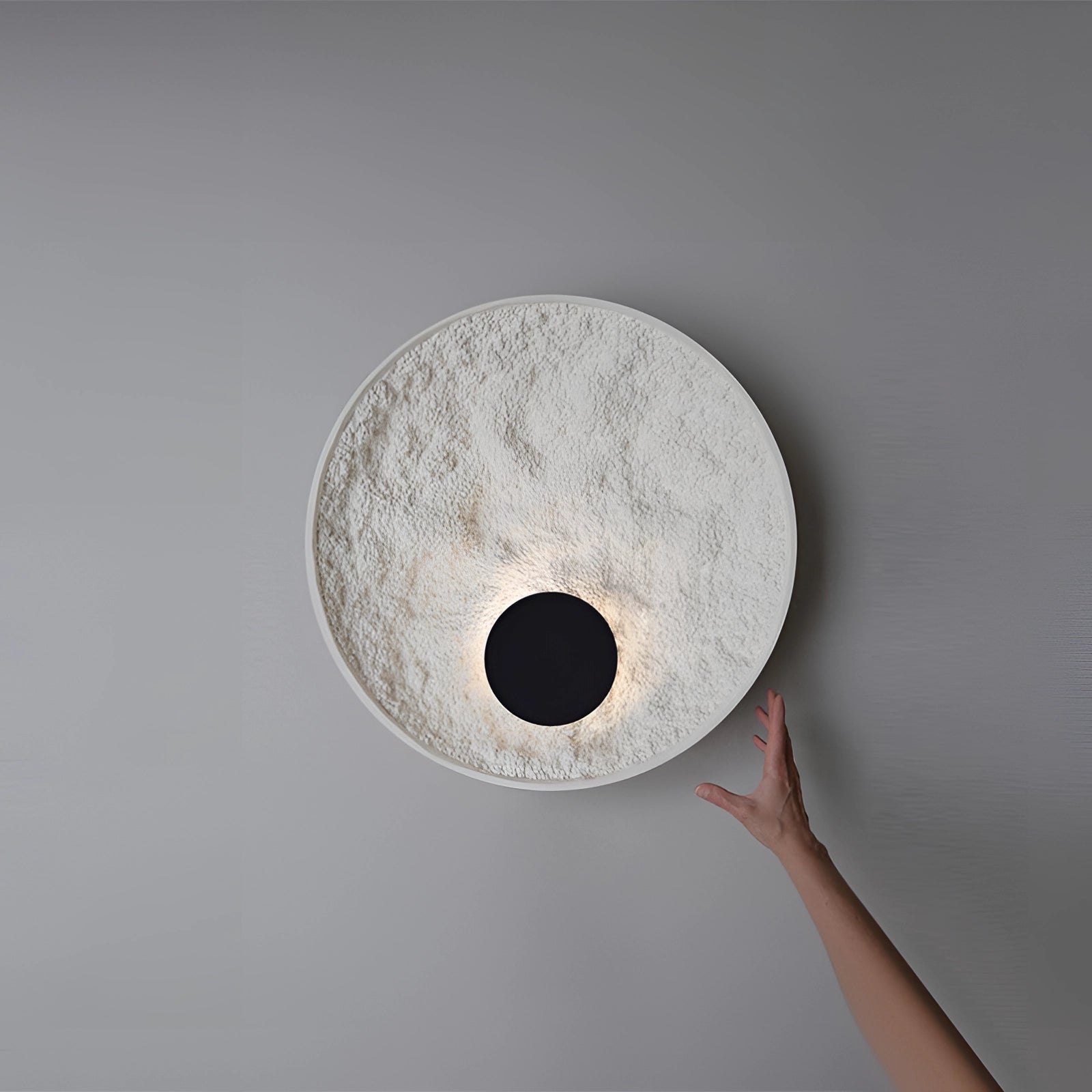 Textured circular wall sconce with a minimalist contemporary design, featuring a beige wood finish and metal accents, mounted on a wall indoors.