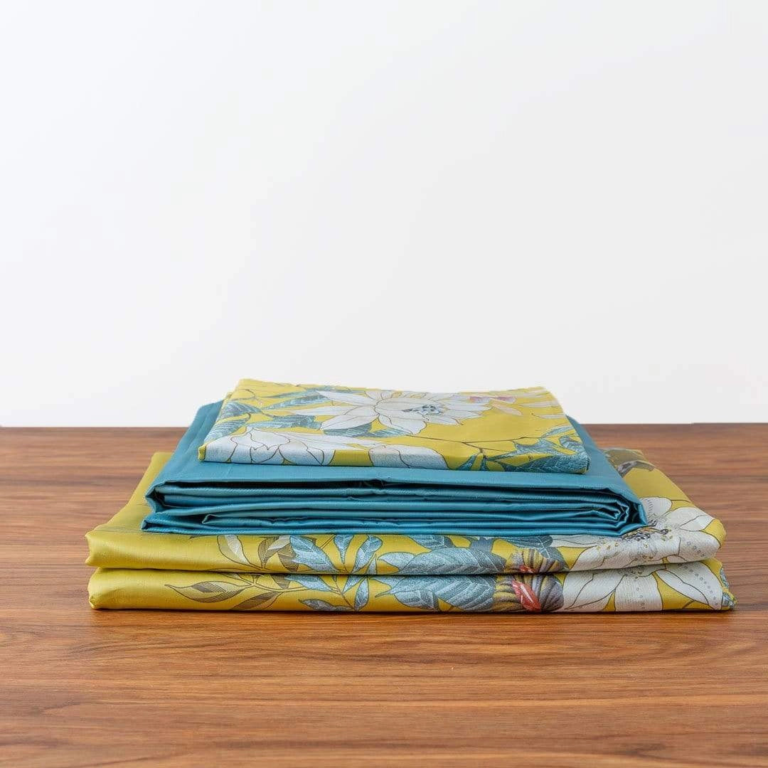 Tropical bedding set featuring a vibrant yellow bird print and floral design on a bedspread, displayed on a wooden bed with hardwood flooring.