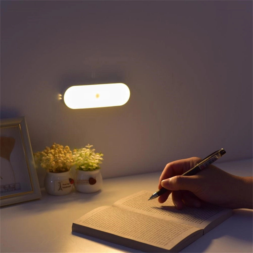 A compact USB LED wireless motion sensor lamp in a minimalist room setting, placed on a wooden surface near a small plant, with neutral-colored tints and shades visible in the background.