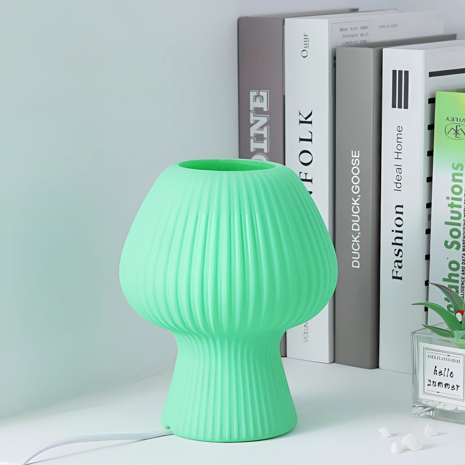 USB Rechargeable Retro Mushroom LED Bedside Lamp in green, shaped like a whimsical mushroom with a soft glow, sitting on a shelf alongside decorative plants and vases.