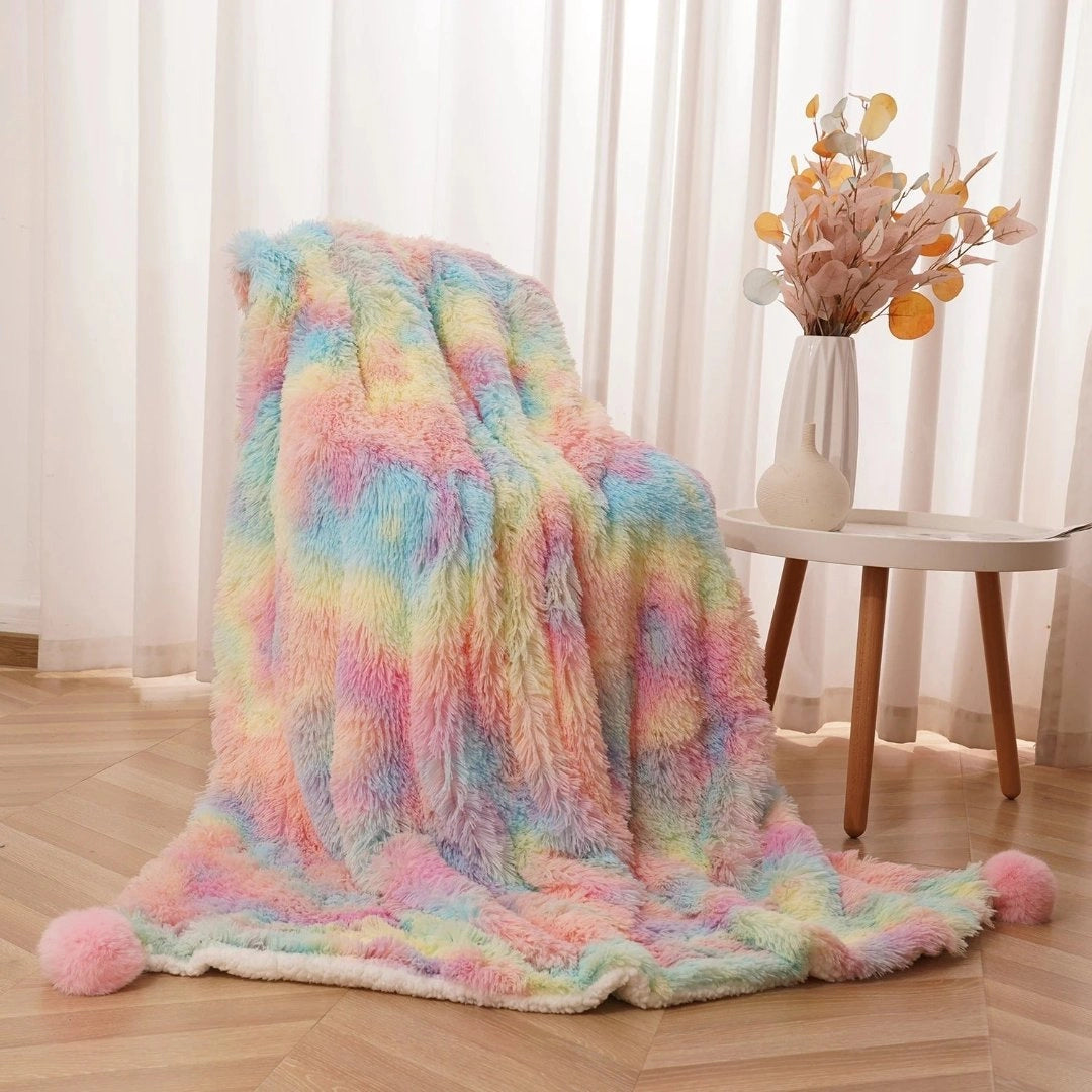 A vibrant multicolor faux fur blanket with a soft pastel palette of purple and pink tones, displayed on a wooden floor, providing a cozy and comfortable aesthetic.