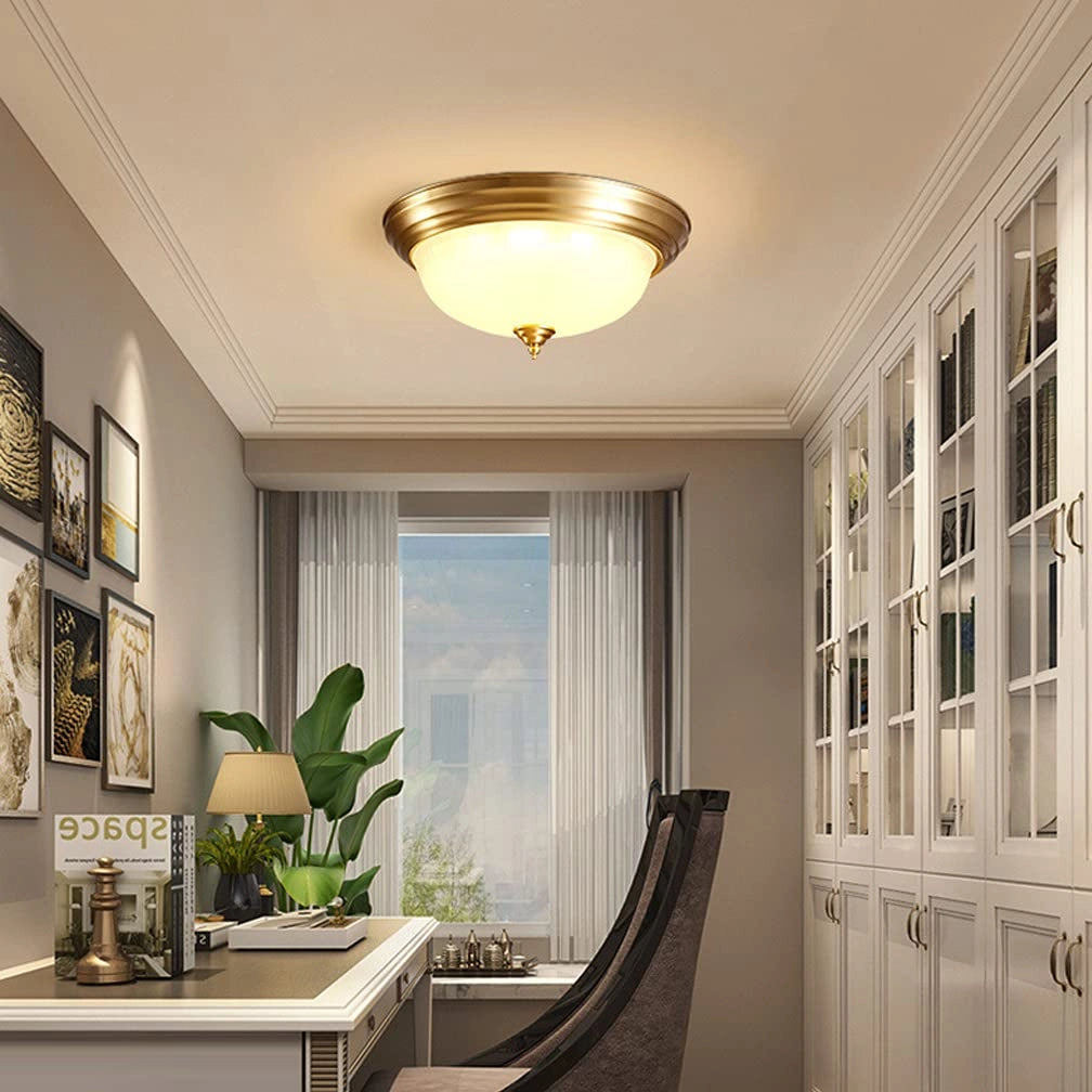 Vintage brass flush mount ceiling light with frosted glass, D 13'', installed in a stylish interior setting with wooden flooring and houseplants.