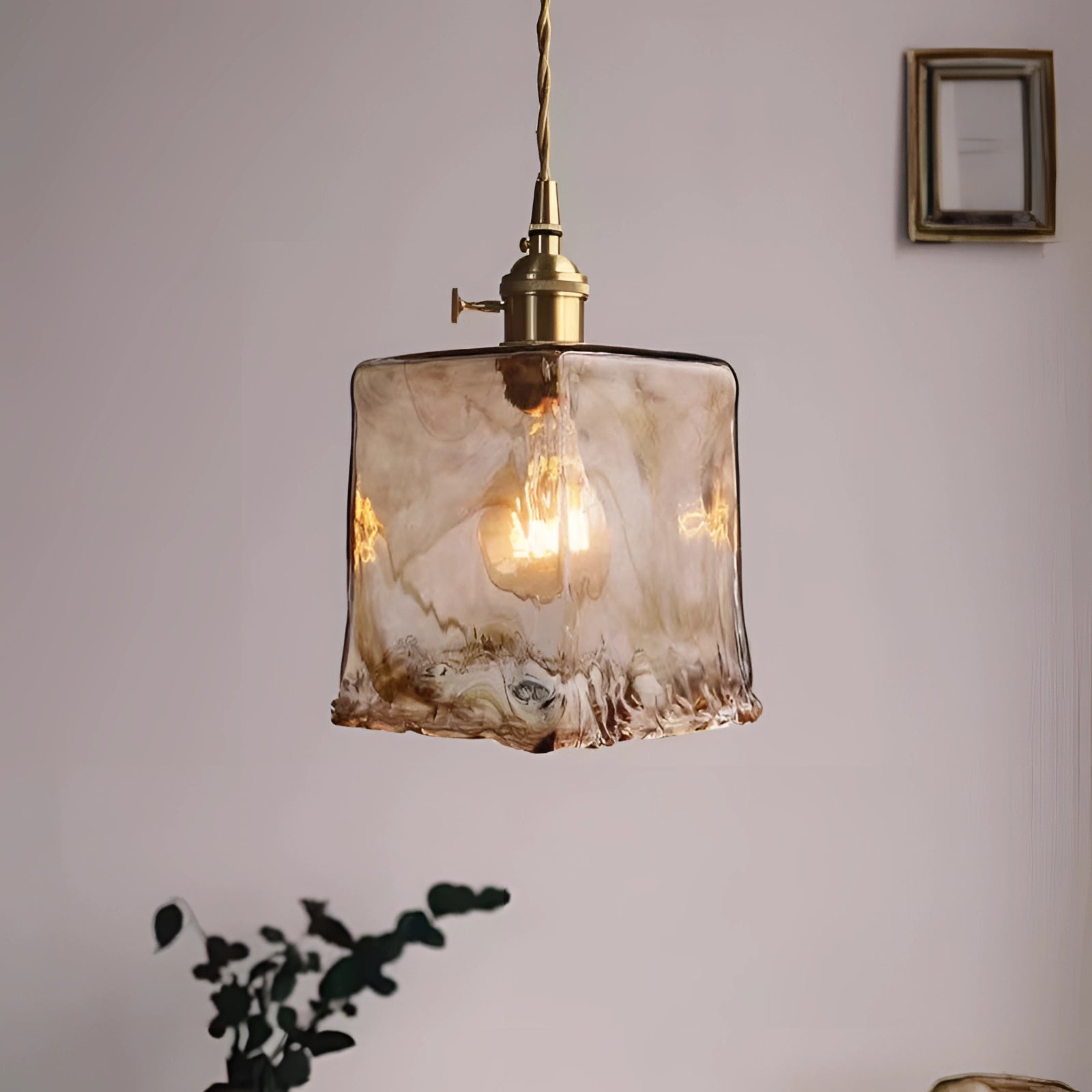 Vintage brass LED pendant light with a handblown glass fixture, showcasing a sleek rectangular design, complemented by natural twig and plant accents.