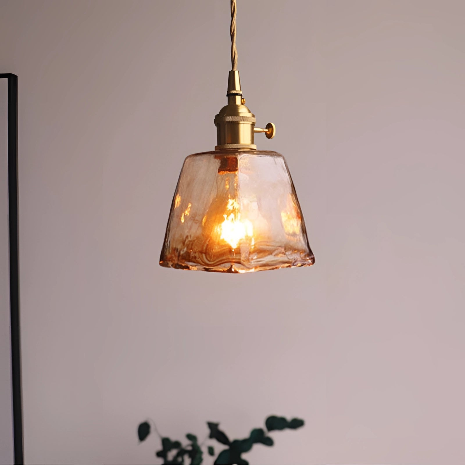 Vintage brass LED pendant light with a handblown glass fixture, featuring a warm amber glow, resembling an elegant lantern design, suspended from a wooden ceiling mount.