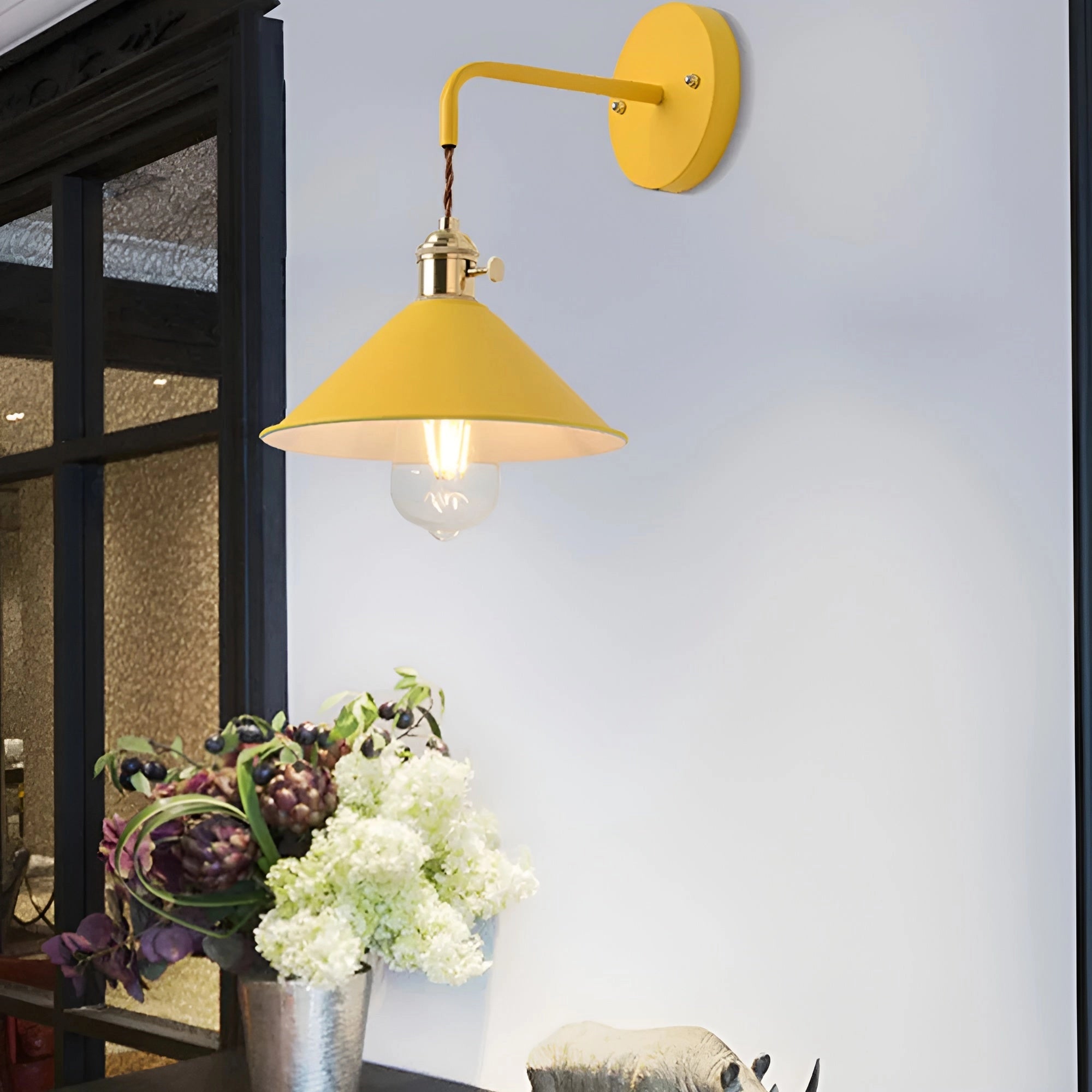Vintage brass and white industrial retro wall sconce with a flower-shaped lamp shade, mounted on a wooden wall, surrounded by houseplants and decorative elements in a stylish interior setting.