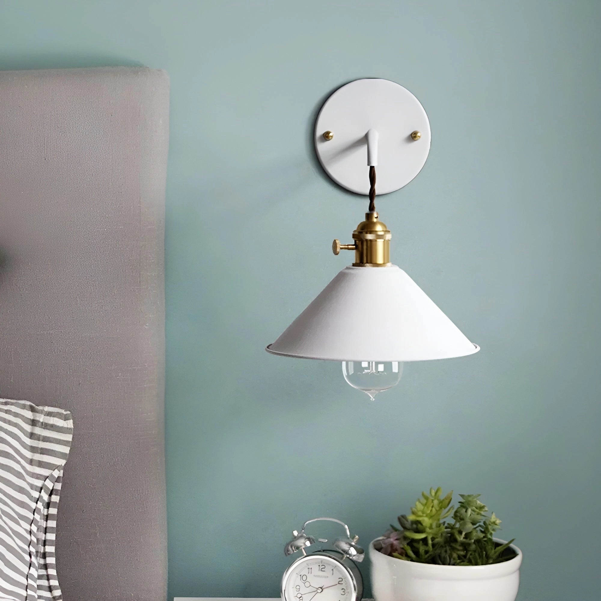 Vintage brass and white wall sconce with an industrial retro design, featuring a white lampshade and brass accents, mounted on a wooden wall, casting warm yellow light in a stylish interior setting.
