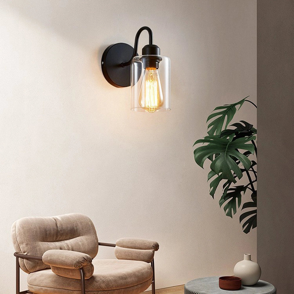 
A vintage Edison bulb wall sconce featuring a black metal frame and clear glass shade, mounted on a wooden wall with a houseplant nearby, enhancing the cozy and stylish interior design.