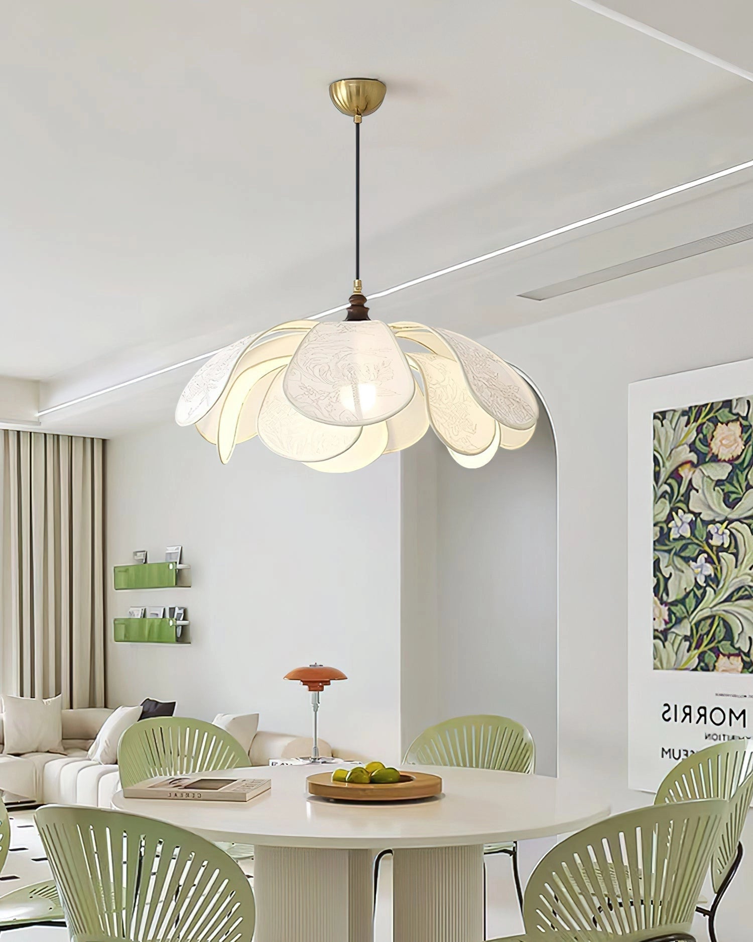 Vintage floral pendant light with etched glass lampshade hanging over a wooden dining table in a stylishly designed interior with chairs, a couch, and large windows.