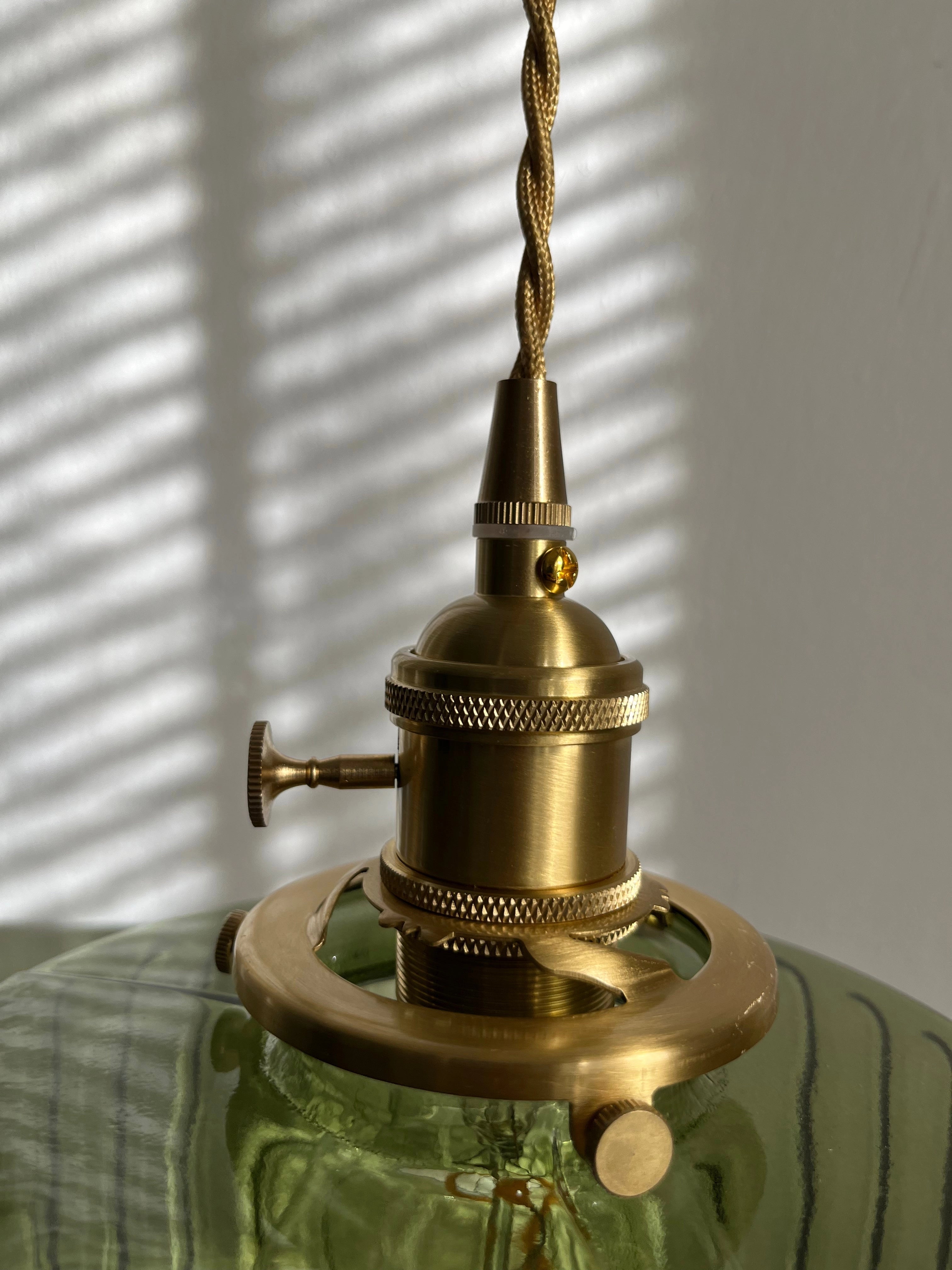 Vintage green glass pendant light with industrial brass fixture, hanging in a kitchen setting.