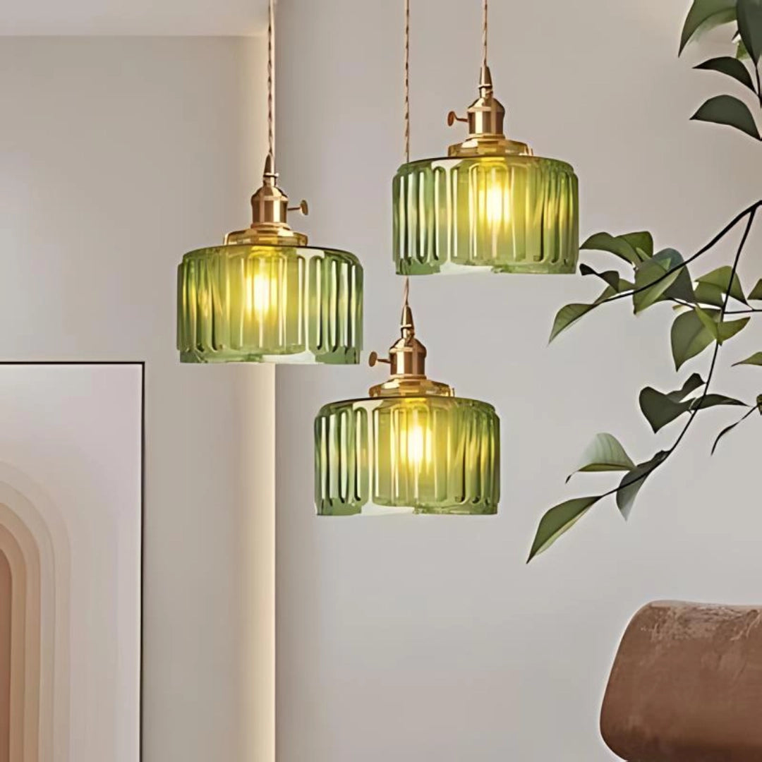 Vintage green glass pendant light with three round ribbed glass shades and antique brass fixtures, hanging in a room with natural elements like wood and plants.