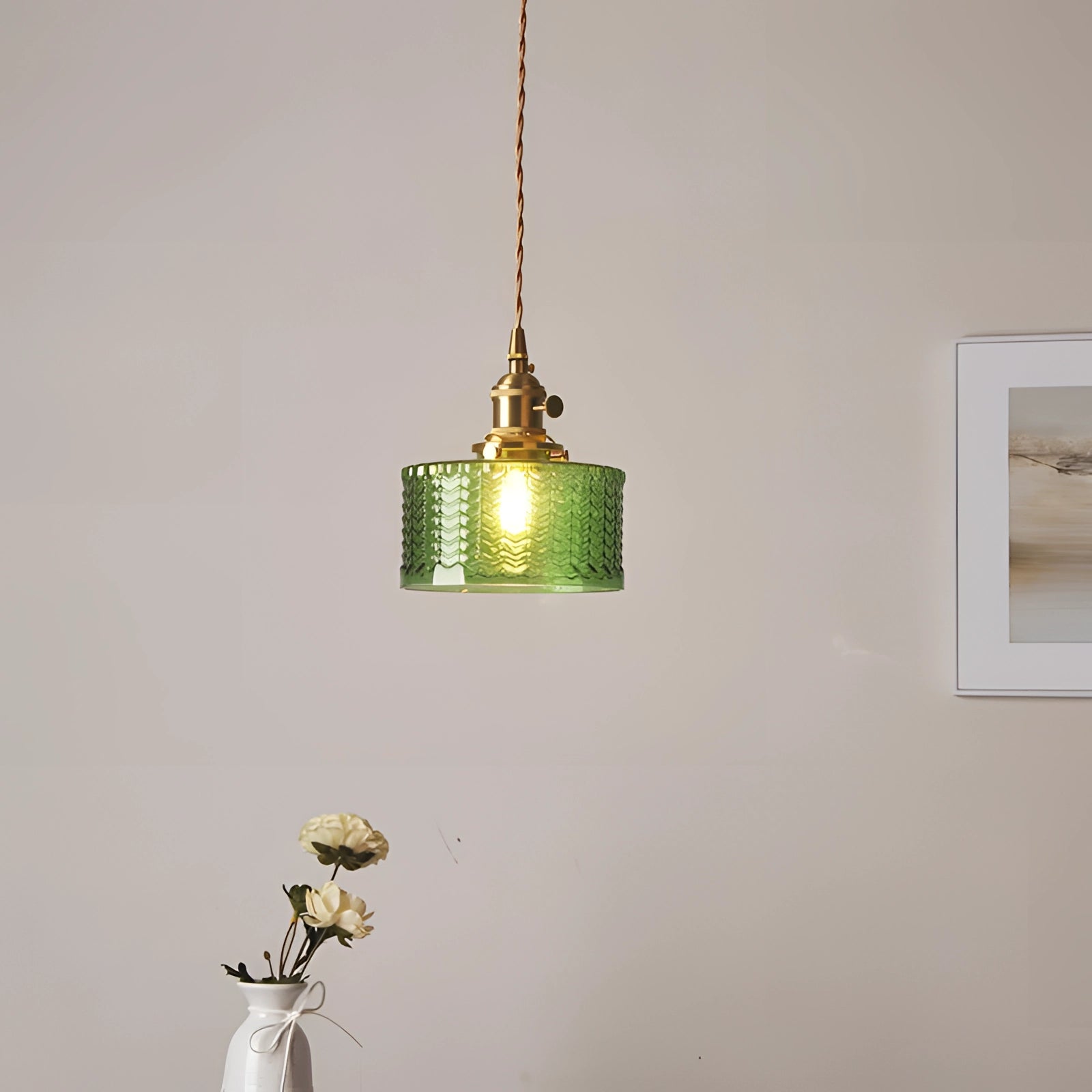 Vintage industrial glass pendant light with green shade and brass fittings, hanging in a rustic setting with wooden elements and plants in the background.