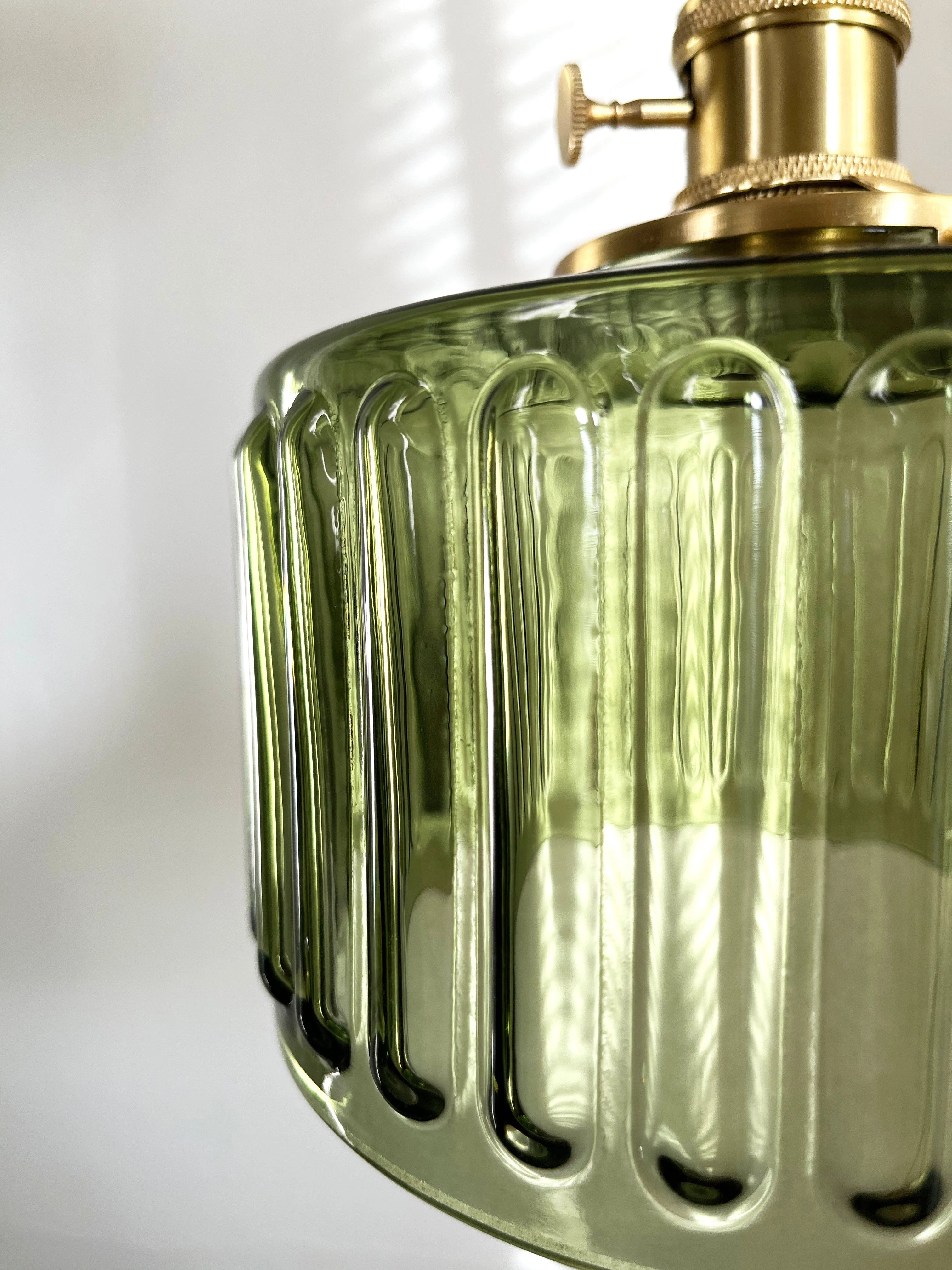 Vintage industrial glass pendant light with a green shade and brass fittings, hanging from a ceiling.
